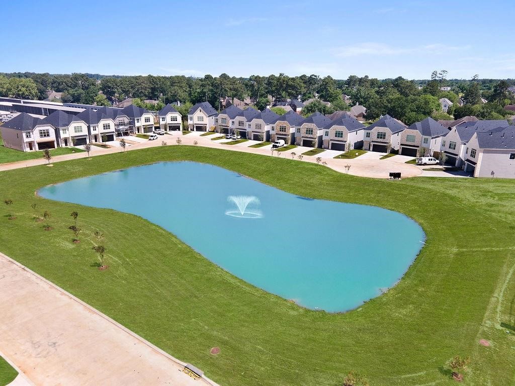 This GATED serene residential neighborhood facing a picturesque pond with a central fountain, surrounded by well-maintained lawns and greenery.