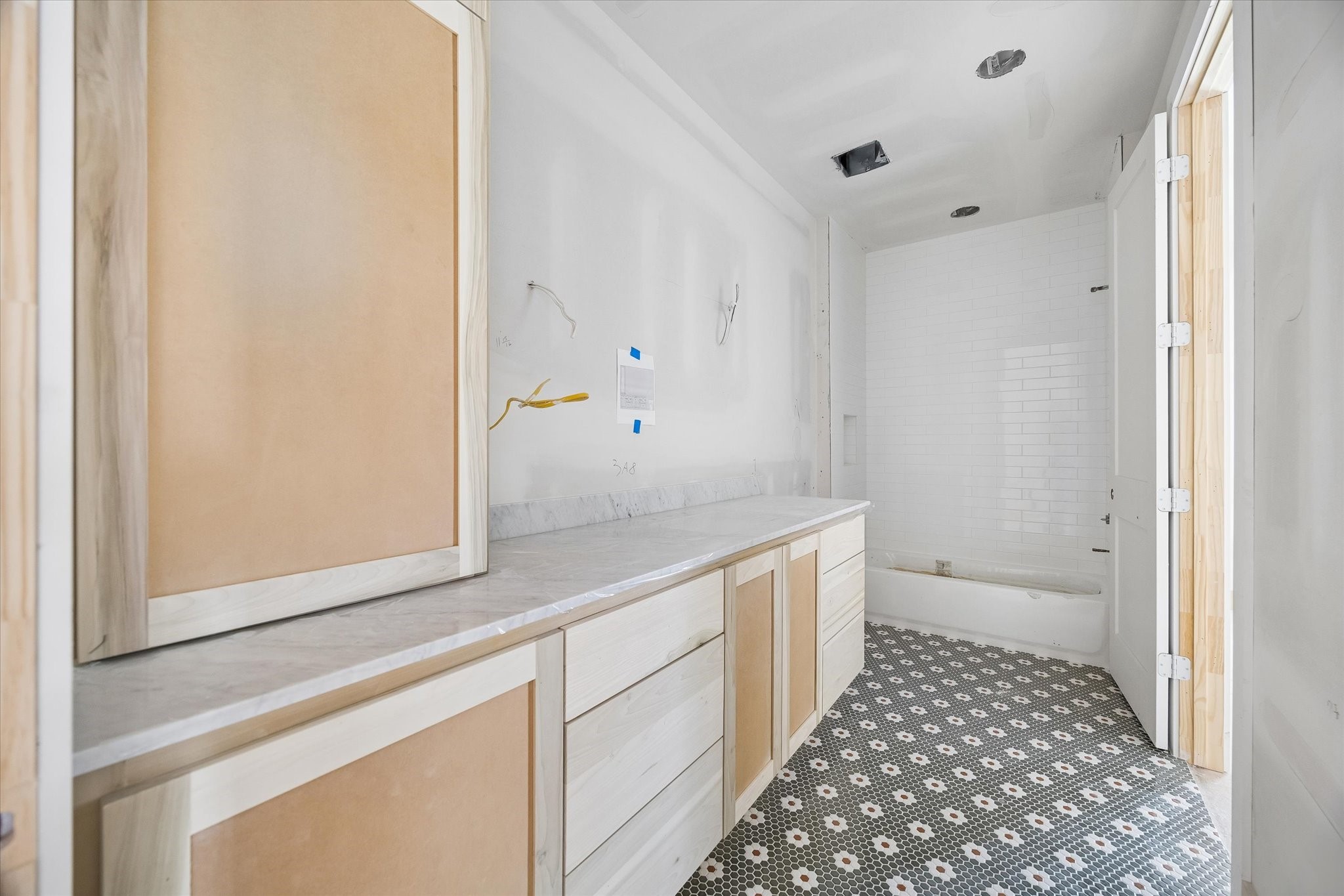 Patterned mosaic tile brings personality to this ensuite bath, balanced by warm custom cabinetry and a long stone topped vanity. Full height shower tile and a built in niche continue the thoughtful finish selections. **Current Construction as of 9/11/26