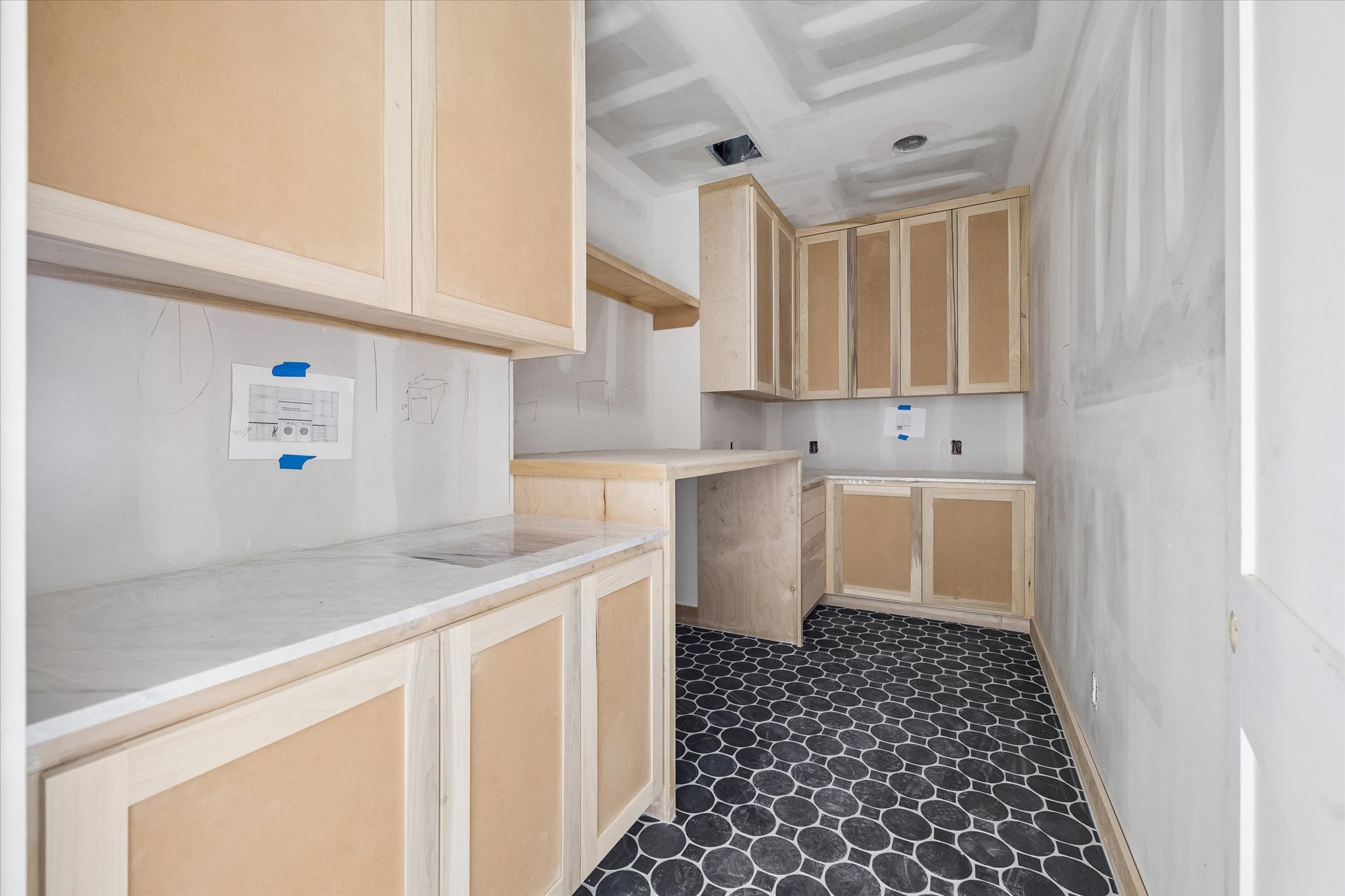Utility room pairs everyday practicality with elevated design, featuring extensive custom cabinetry, stone countertops and a dedicated folding or workspace area. Bold dark mosaic flooring gives this hardworking space a distinctive finish. **Current Construction as of 9/11/26