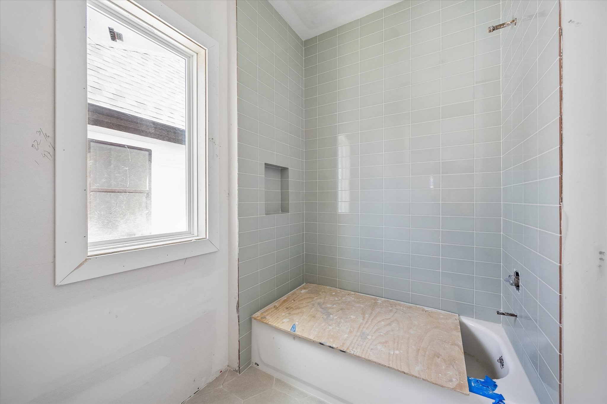 Jack and Jill bath features a tub and shower combination wrapped in soft green tile, with a built in niche for everyday essentials. A nearby window brings natural light into the bathing area. **Current Construction as of 9/11/26