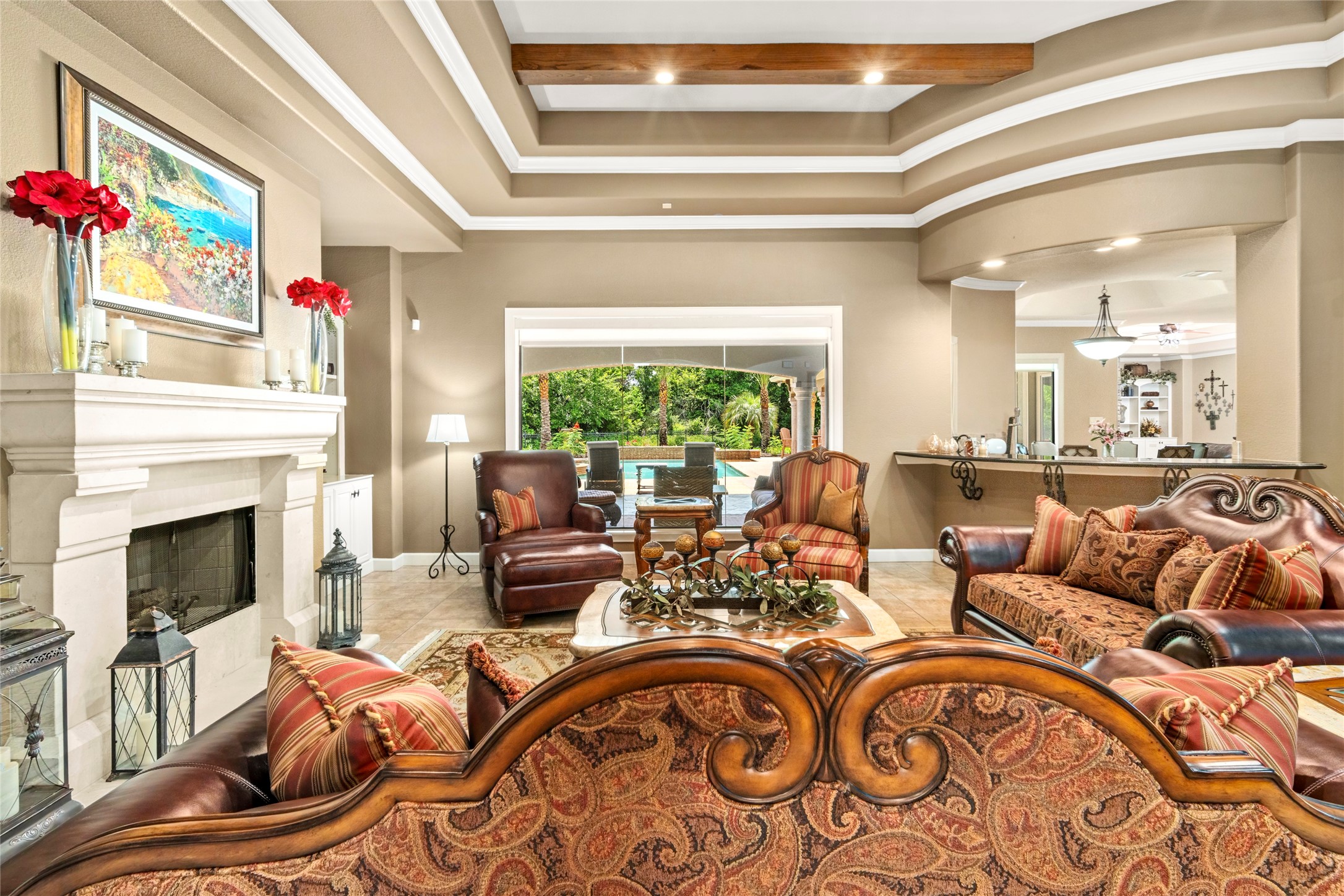 The formal living room has a wall of glass overlooking the lush backyard oasis. One of the five exquisitely detailed fireplaces in this room and a view into the wet bar area which is perfectly situated between the kitchen and family room.