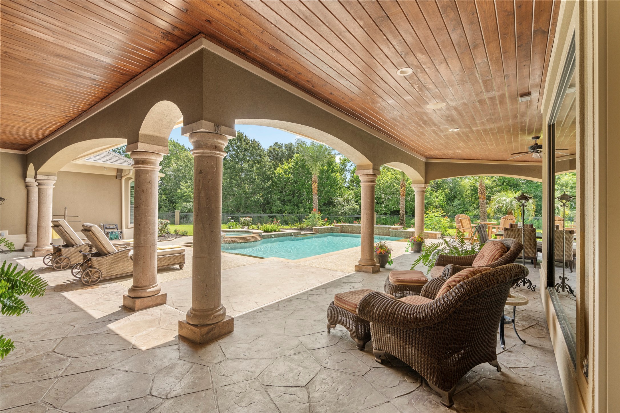 The outdoor area offers stone columns, stained bead board ceilings, abundant covered lounging areas, and sweeping views of the pool and spa.