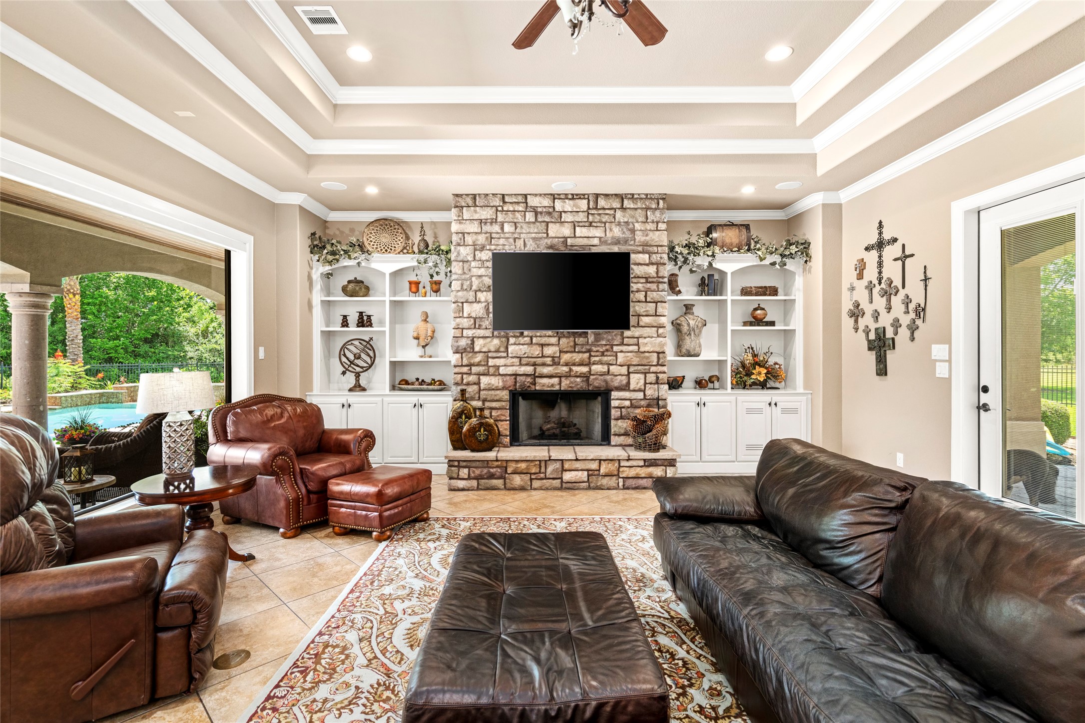 The family room off of the kitchen with a wall of glass blurs indoor outdoor living, while custom built-ins and a stone fireplace make it an instant favorite spot.