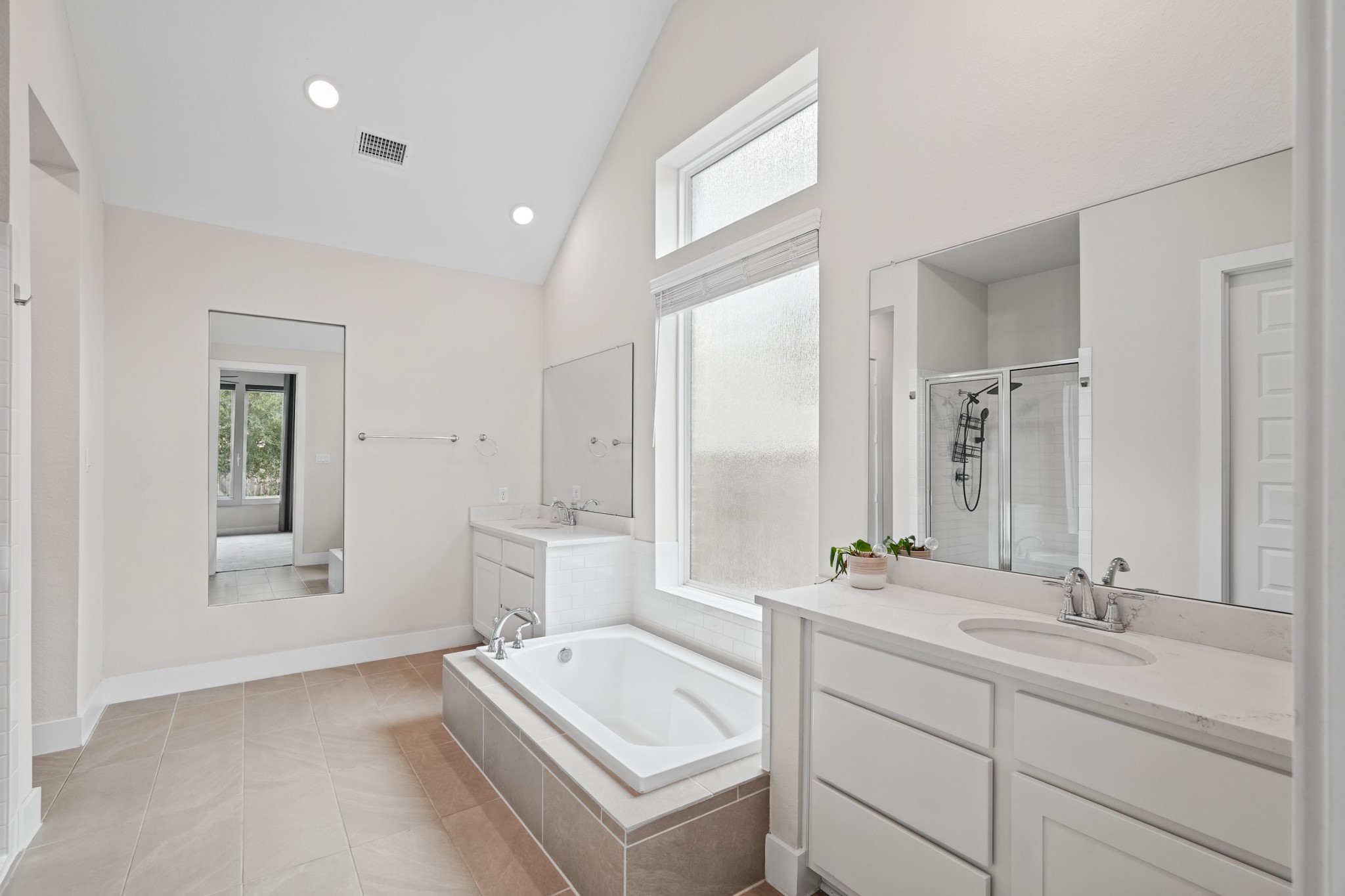 Spa-style primary bath features a freestanding soaking tub set beneath a window, paired with a separate vanity and clean, contemporary tile and fixture selections throughout.