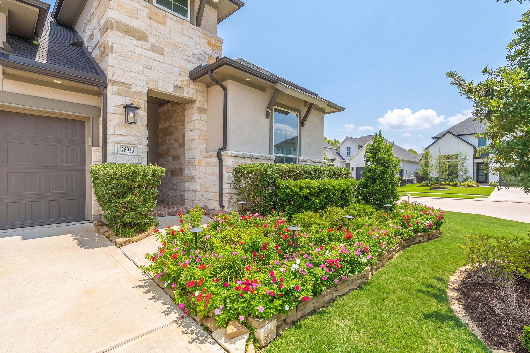 Close-up of the entry and garage approach, where stone accents, carriage-style lighting and flowering beds create a polished, welcoming first impression for arriving guests.