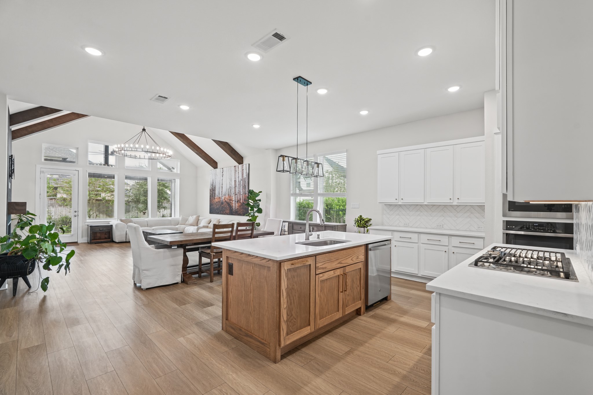 A soaring vaulted ceiling with exposed wood beams rises above the kitchen and living area, giving this open floor plan a bright, airy feel rarely found in a single story.