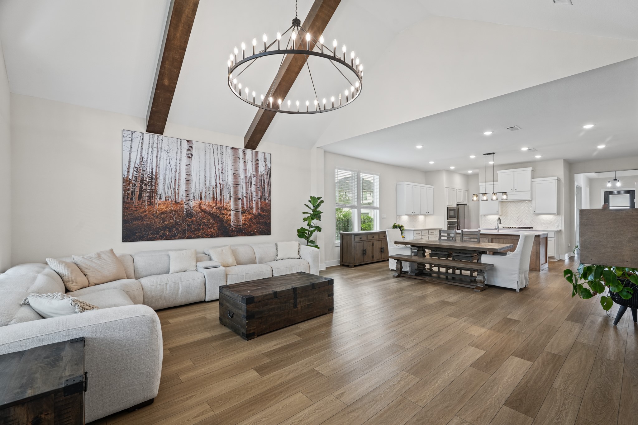 Oversized windows and a statement light fixture brighten the living area, where the vaulted ceiling and exposed beams add architectural warmth, height and a sense of craft.
