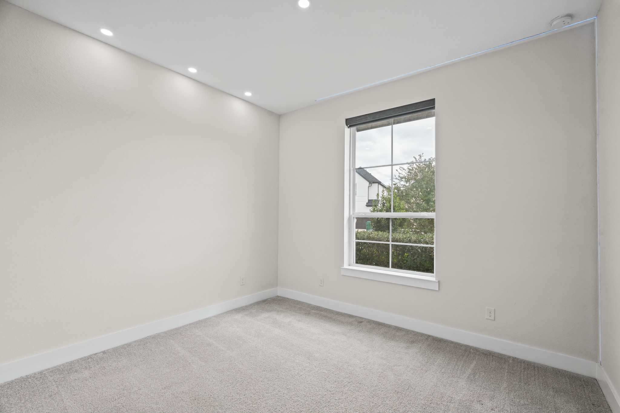 Bright bedroom with a large window, neutral carpet and recessed lighting - flexible enough to serve as a guest suite, a playroom or a comfortable second home office.