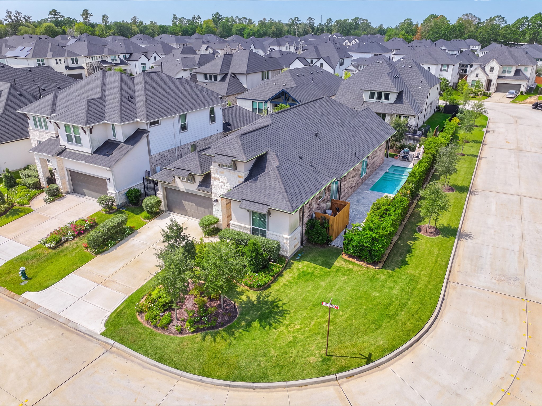 Overhead view of the property showing the pool, covered patio and generous corner lot, with sidewalk-lined streets and well-kept homes throughout the surrounding community.