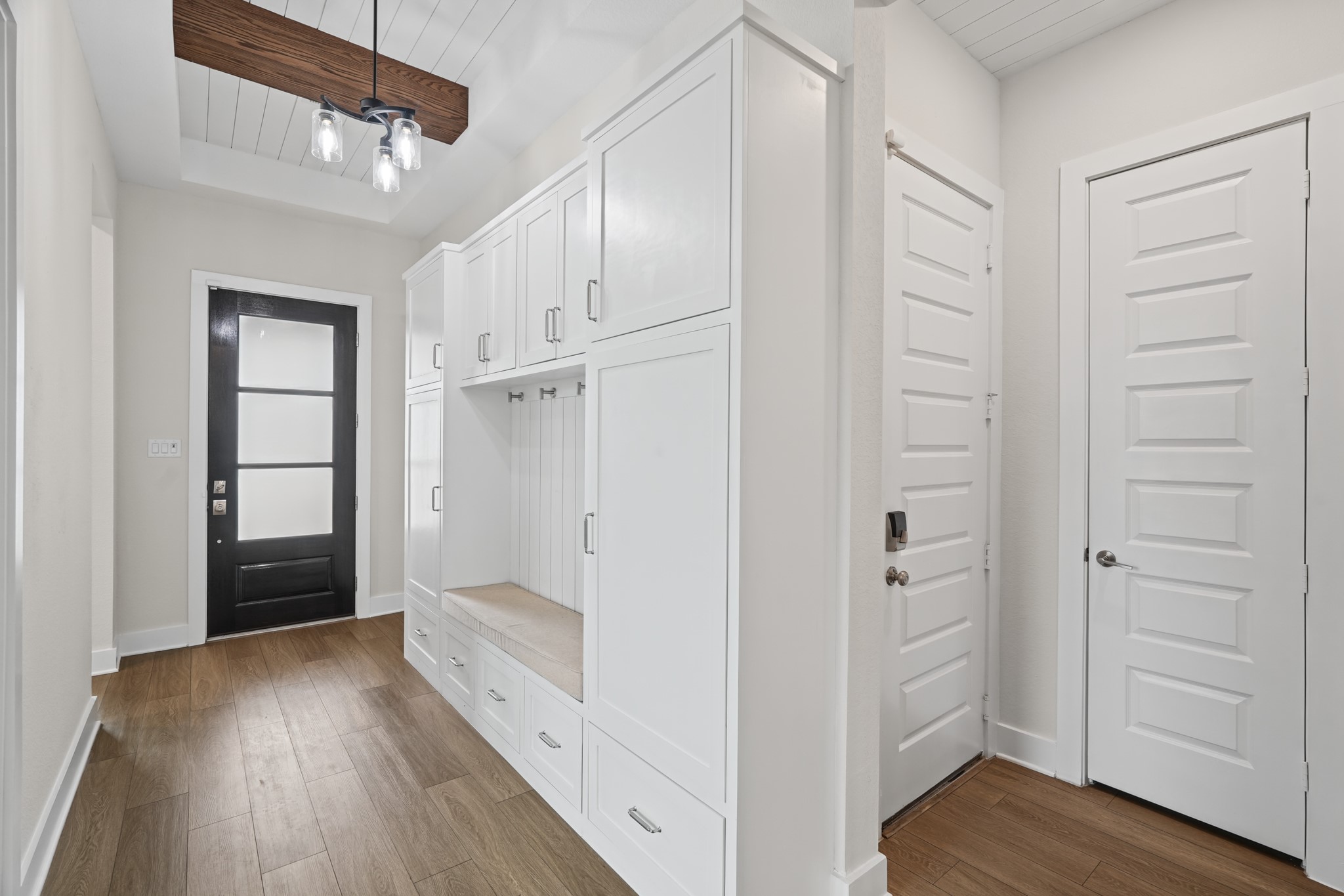 The entry hall welcomes you with a glass-paned front door, a built-in bench with hooks above and wide-plank flooring leading into the home's open central living space.