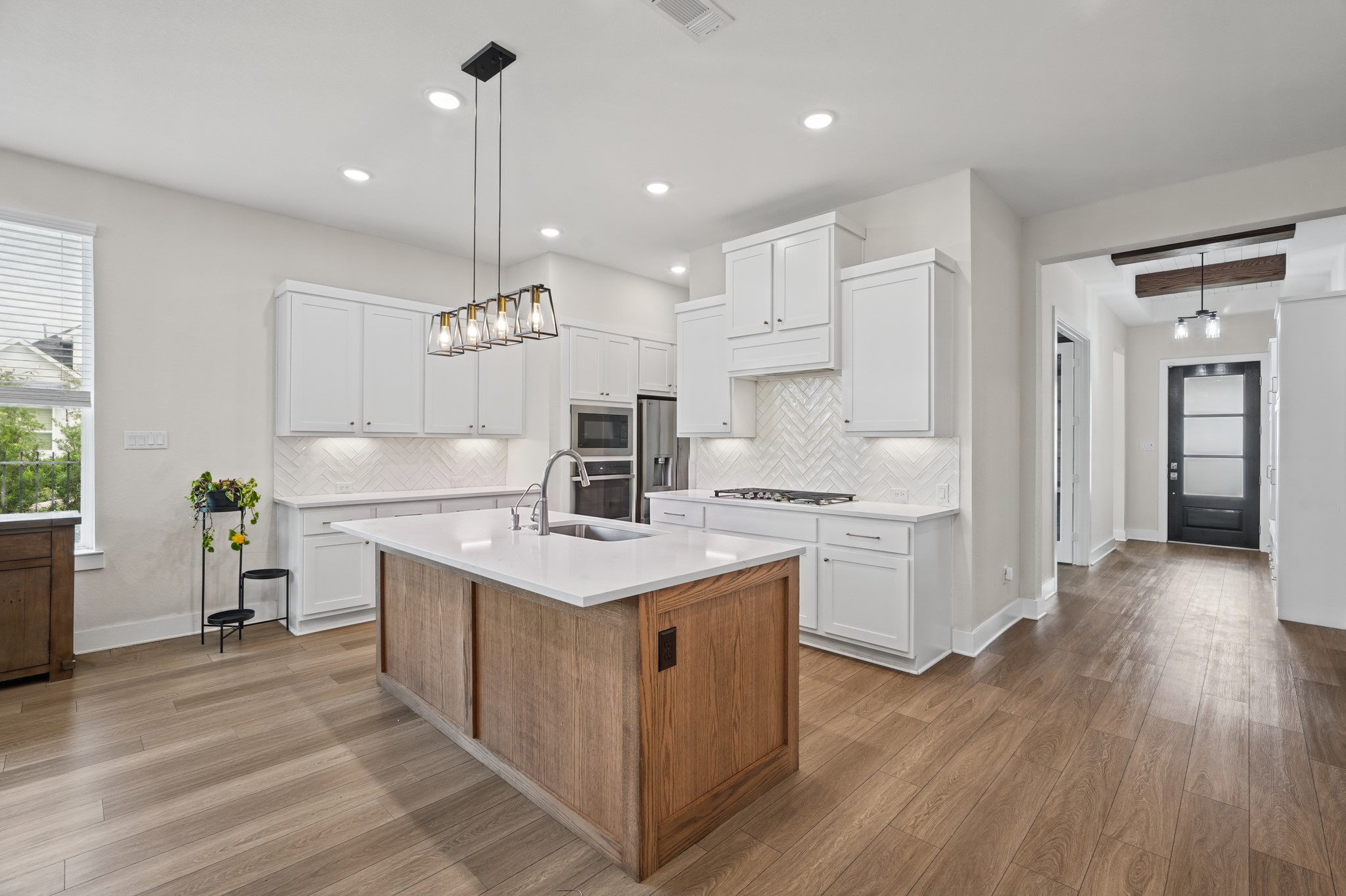 Generous center island offers prep space and casual seating, paired with crisp white cabinetry, designer pendant lighting and a clean, timeless finish palette throughout.