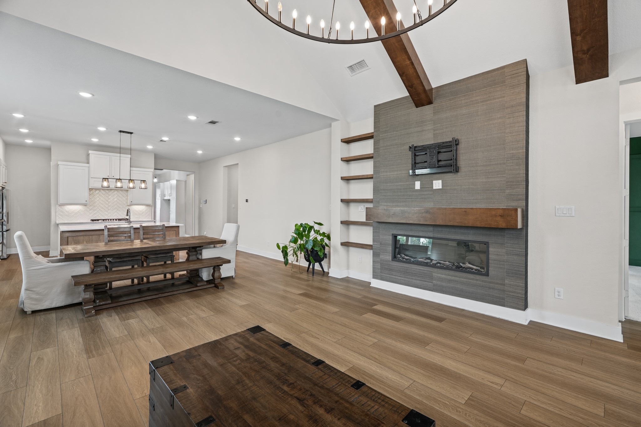 A wide view across the living and dining areas shows how the fireplace wall, beamed ceiling and open kitchen work together as one comfortable, flexible gathering space.
