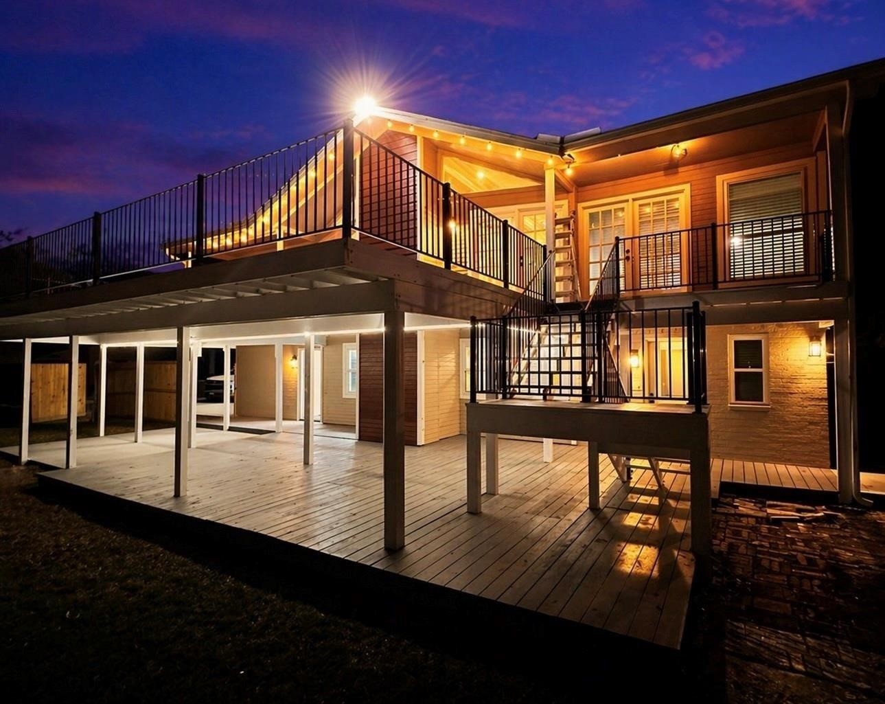 Expansive upper and lower decks, modern railings, and warm exterior lighting that creates an inviting glow at dusk.