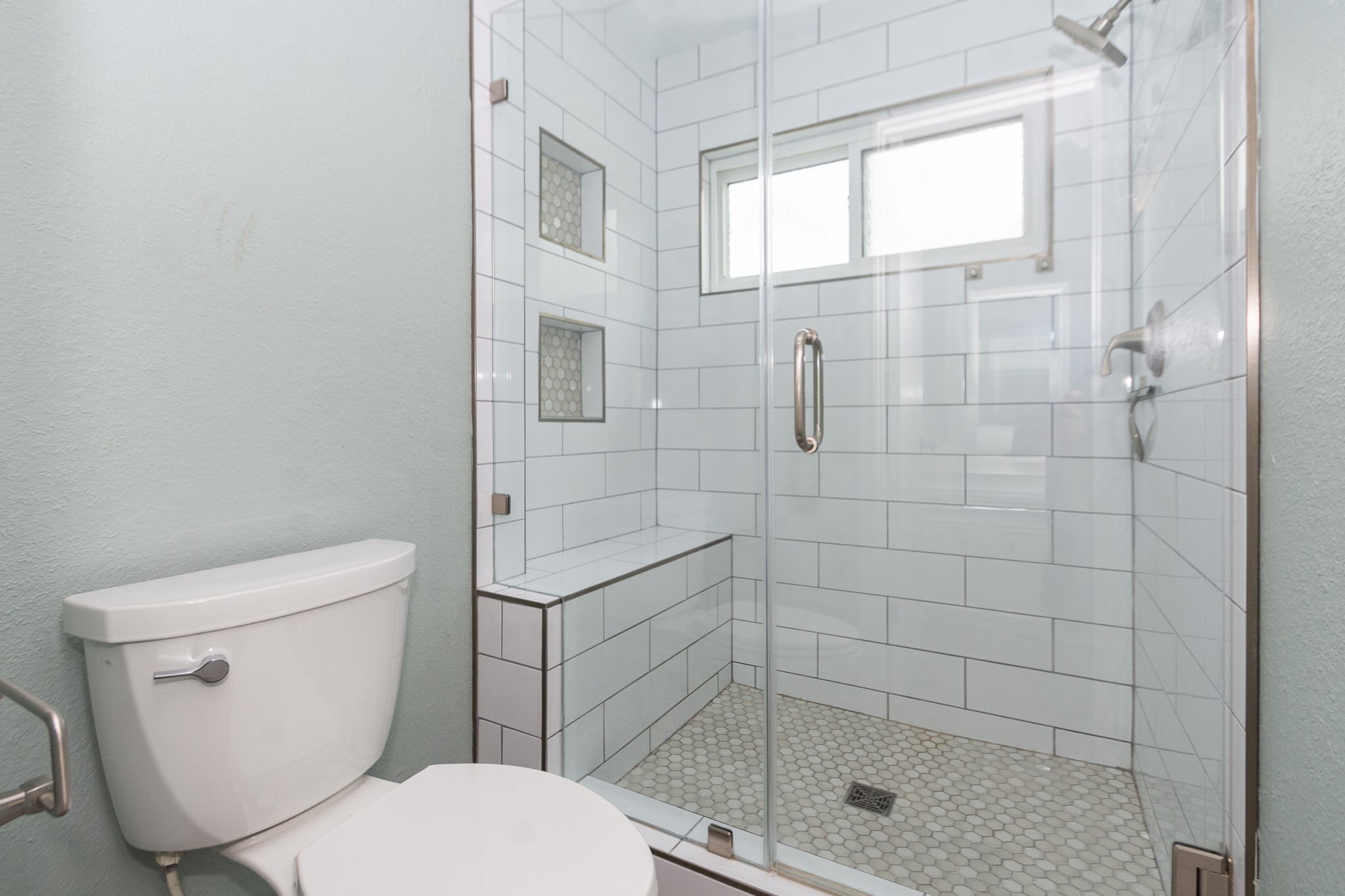 Primary Bathroom Glass-enclosed stand-up shower with a built-in bench, dual recessed niches, and fresh subway tile.