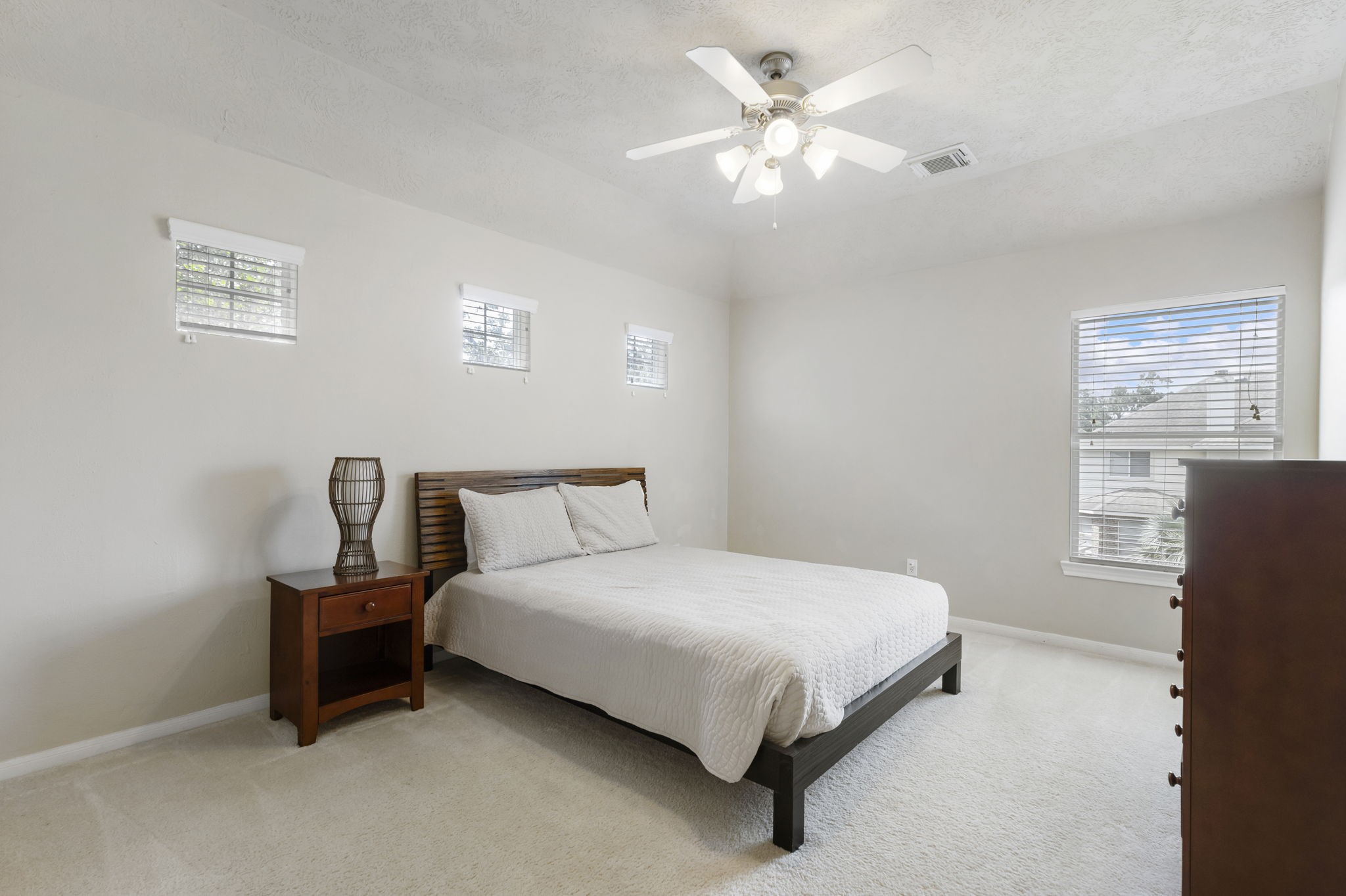 This generously sized secondary bedroom features soaring ceilings, a ceiling fan, and multiple windows that create a bright, open, and airy feel throughout the room.