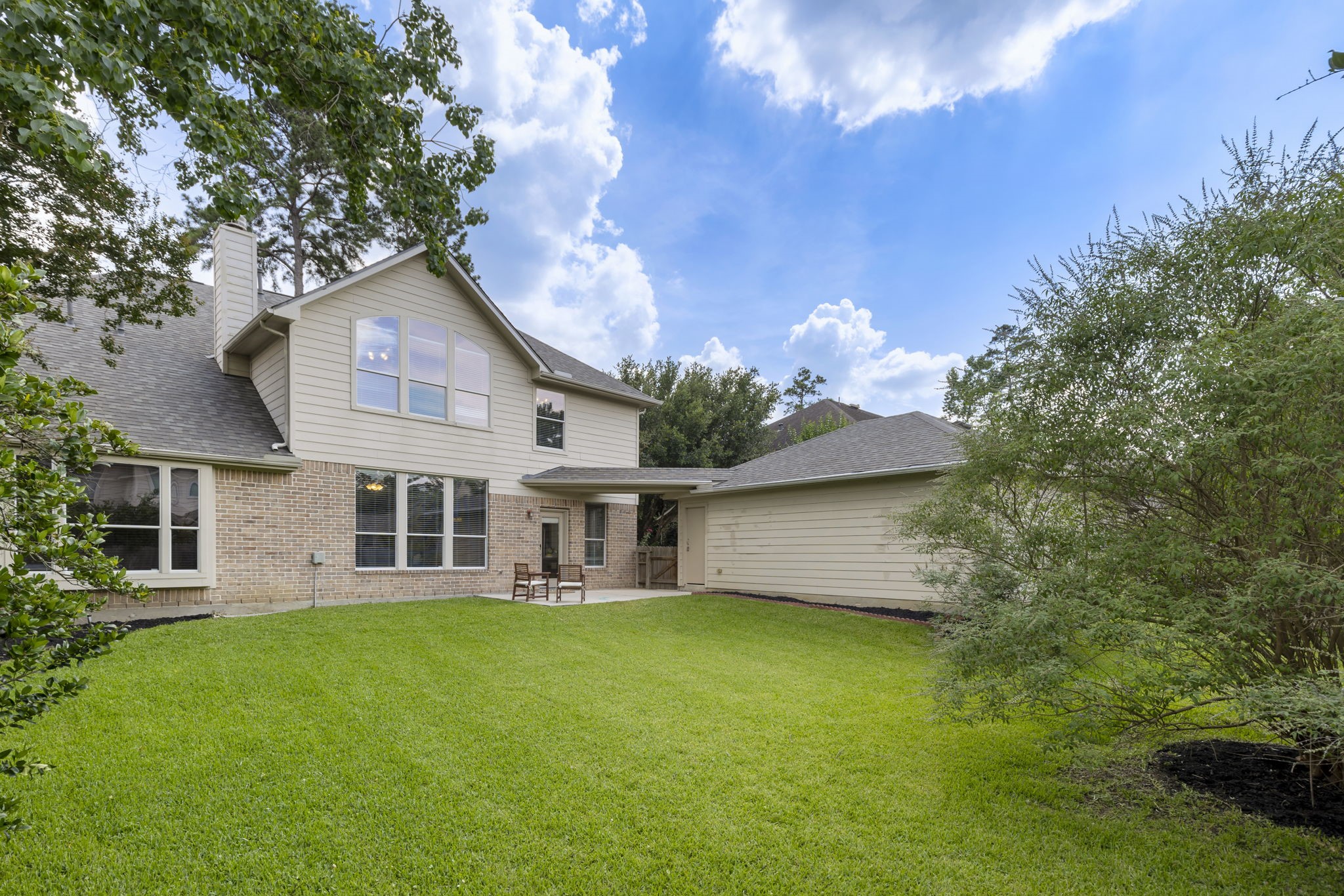 A beautiful view of the home showcasing the generous backyard space, mature greenery, and large windows that bring natural light into the home.