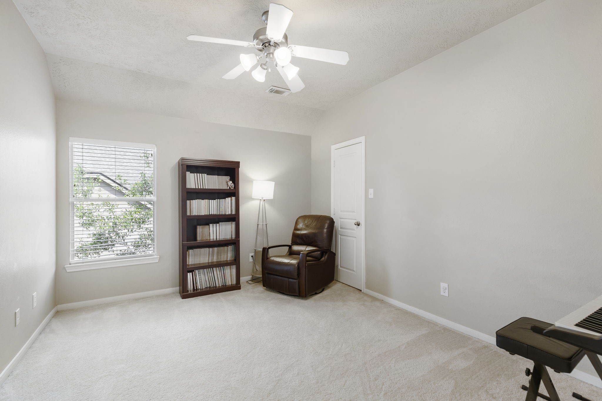 This spacious secondary bedroom features a ceiling fan, large window that fills the room with natural light, and plenty of space to serve as a comfortable bedroom, private office, or creative space.