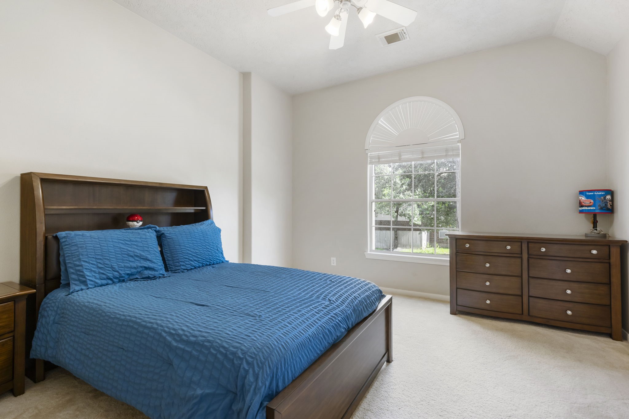 This bright secondary bedroom showcases a beautiful arched window, elevated ceilings, and a ceiling fan while still offering plenty of room for furniture and personalization.