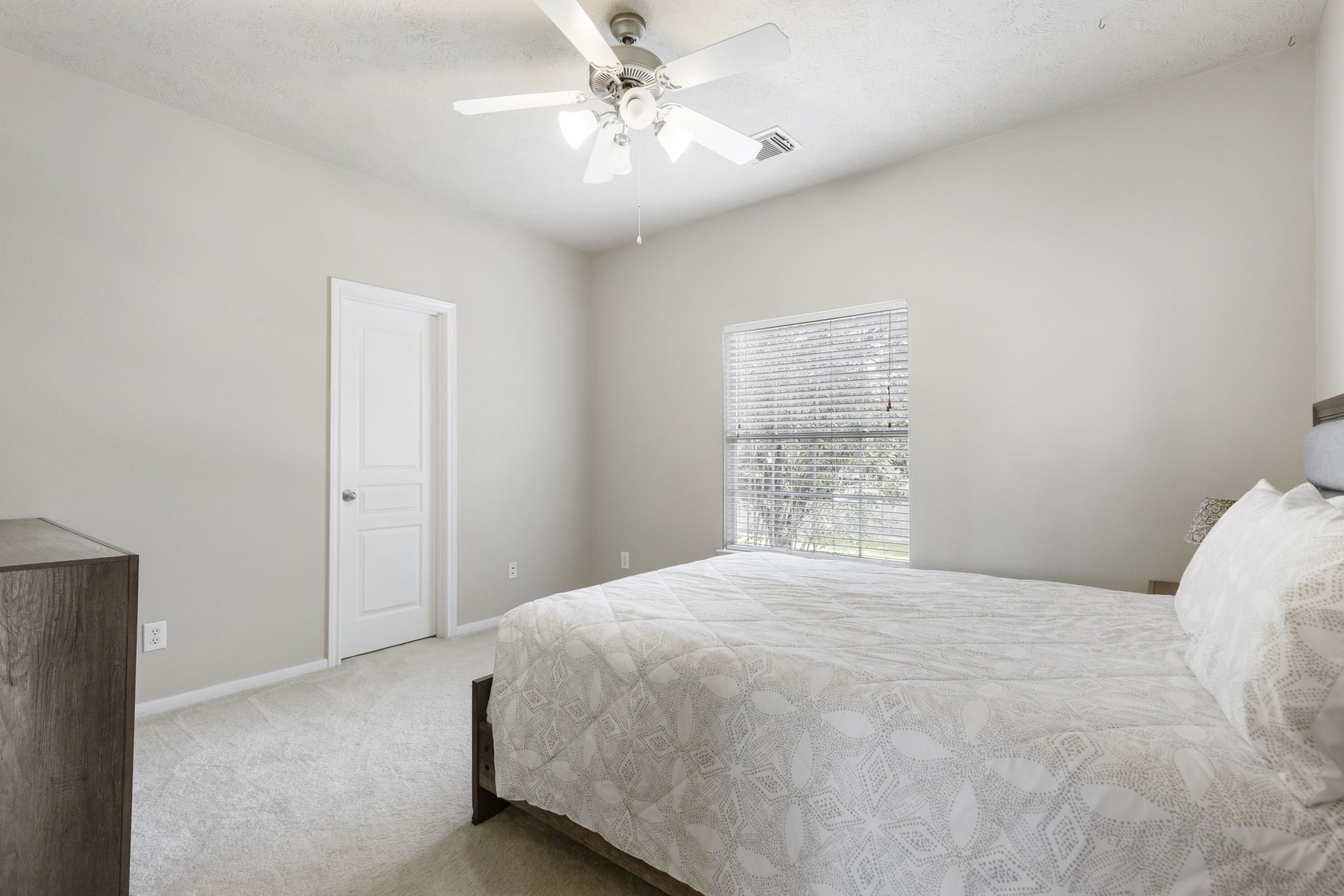 This inviting secondary bedroom offers a comfortable layout with a ceiling fan, neutral finishes, and a large window overlooking the backyard.