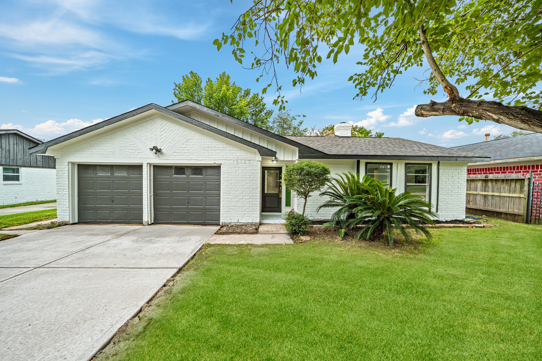 Charming single-story home with a classic white brick exterior, featuring a double garage and a well-maintained front yard surrounded by mature trees.