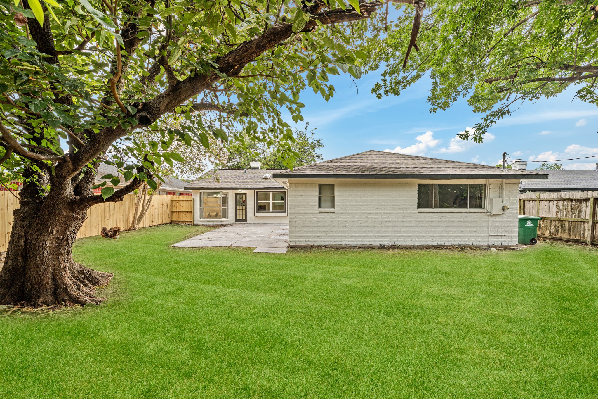 Charming backyard with a spacious lawn, mature tree, and a cozy patio area, perfect for outdoor gatherings.
