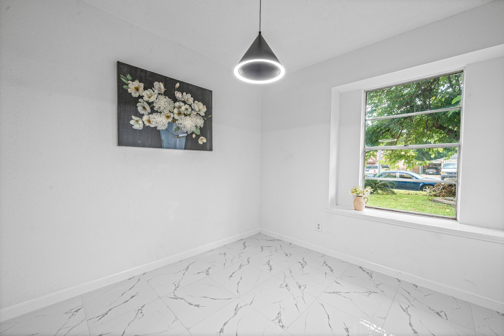 Bright and airy room with white marble flooring, a modern pendant light, and a large window offering plenty of natural light. Bright and airy room with white marble flooring, a modern pendant light, and a large window offering plenty of natural light.