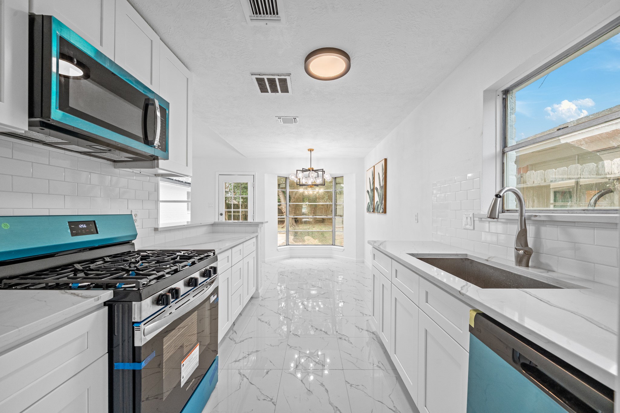 Sleek modern kitchen with stainless steel appliances, white cabinetry, and elegant marble countertops. Ample natural light flows through large windows, highlighting the spacious layout perfect for entertaining.