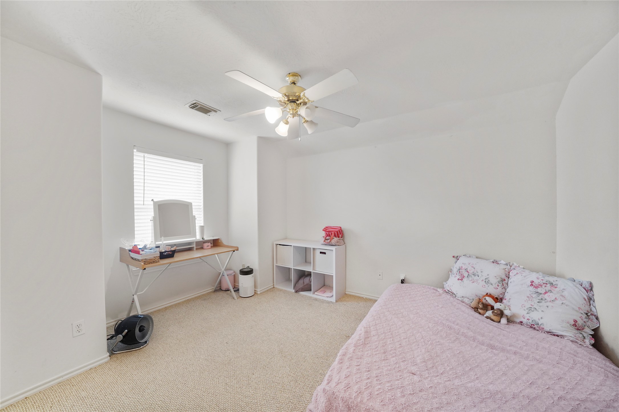 This secondary bedroom has a bright window, ceiling fan, and a neutral backdrop that can grow with changing needs.