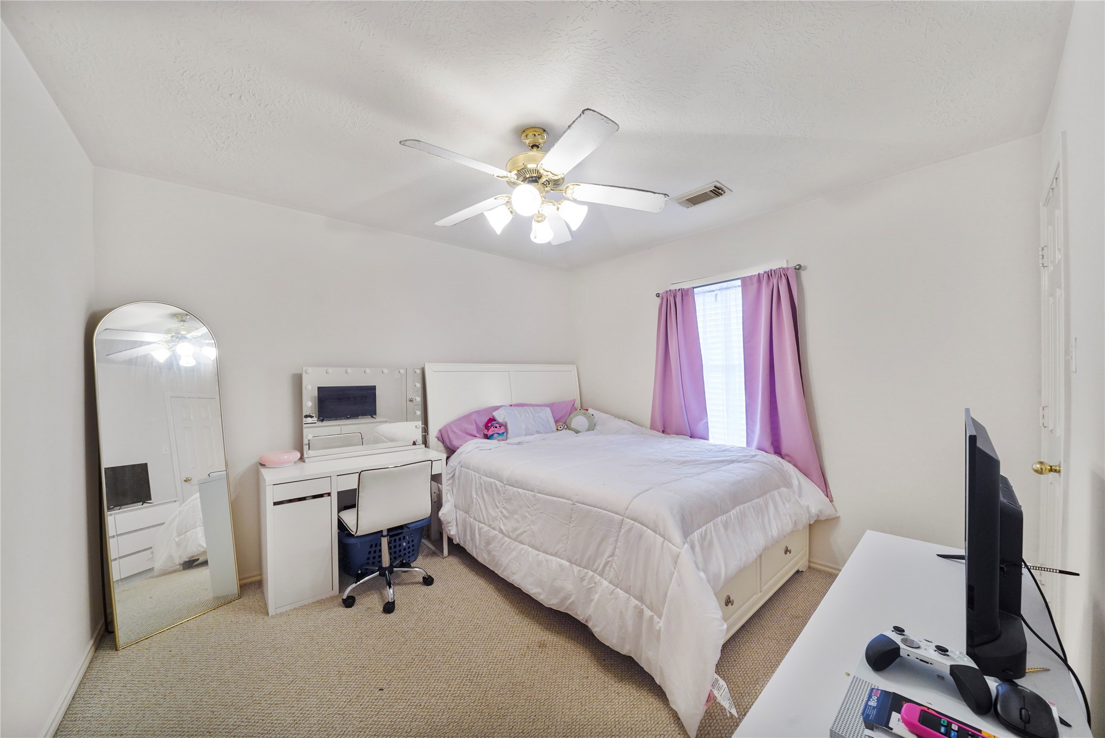 Another secondary bedroom offers a comfortable setup for guests, hobbies, or a home office, with soft carpet and a cheerful window.