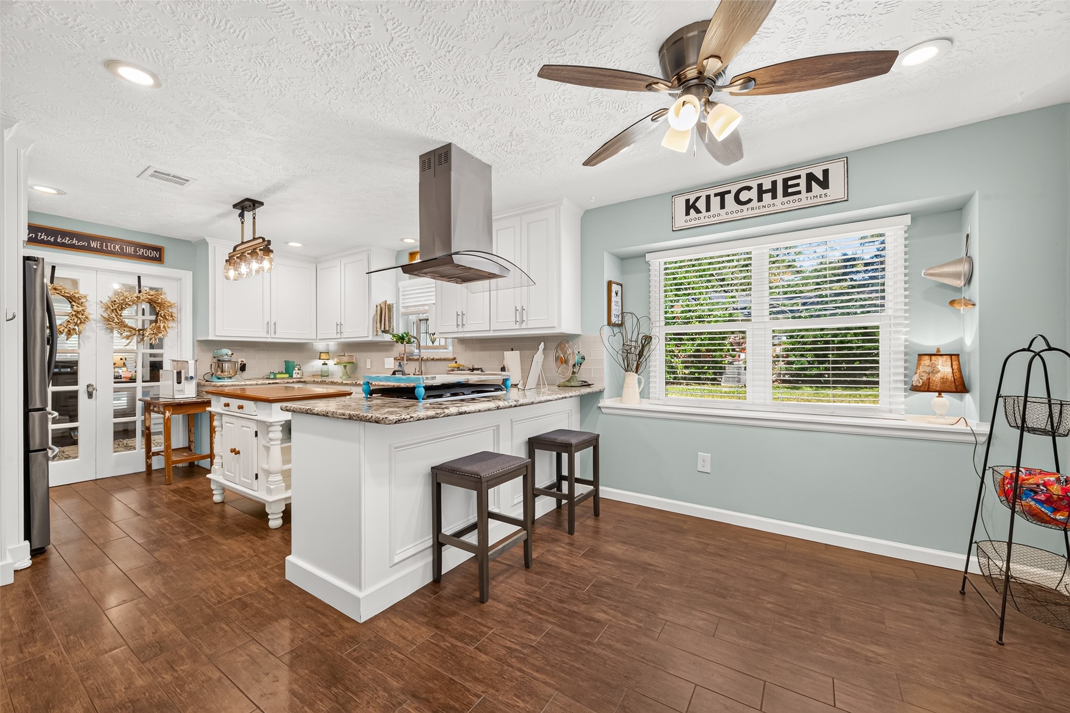 VIEW OF THE OFFICE WITH THE VINTAGE GLASS DOORS AND OF THE KITCHEN AND BREAKFAST ROOM; LOTS OF CUSTOM SLOW CLOSING CABINETS, GAS COOKTOP BUILT IN, ISLAND INCLUDED AND SPACIOUS BREAKFAST ROOM WITH A NEW CEILING FAN AND NEW FARMHOUSE LIGHT FIXTURE OVER THE ISLAND