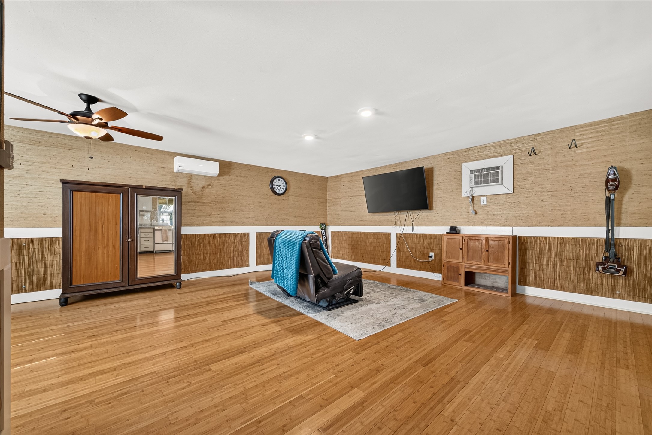 ANOTHER VIEW OF THE POOL HOUSE. WINDOW UNIT WAS ALREADY THERE AND IT DOES WORK. MINI-SPLIT UNIT OFFERS A REMOTE THERMOSTAT; PLENTY OF SPACE FOR A POOL TABLE OR GAME TABLES OR SET UP FOR A LIVING QUARTERS. (TV IS EXCLUDED) THE VINTAGE ARMOIRE WILL REMAIN WITH HOME AS CLOSET SPACE. LOOK AT THE BEAUTIFUL BAMBOO FLOORS!