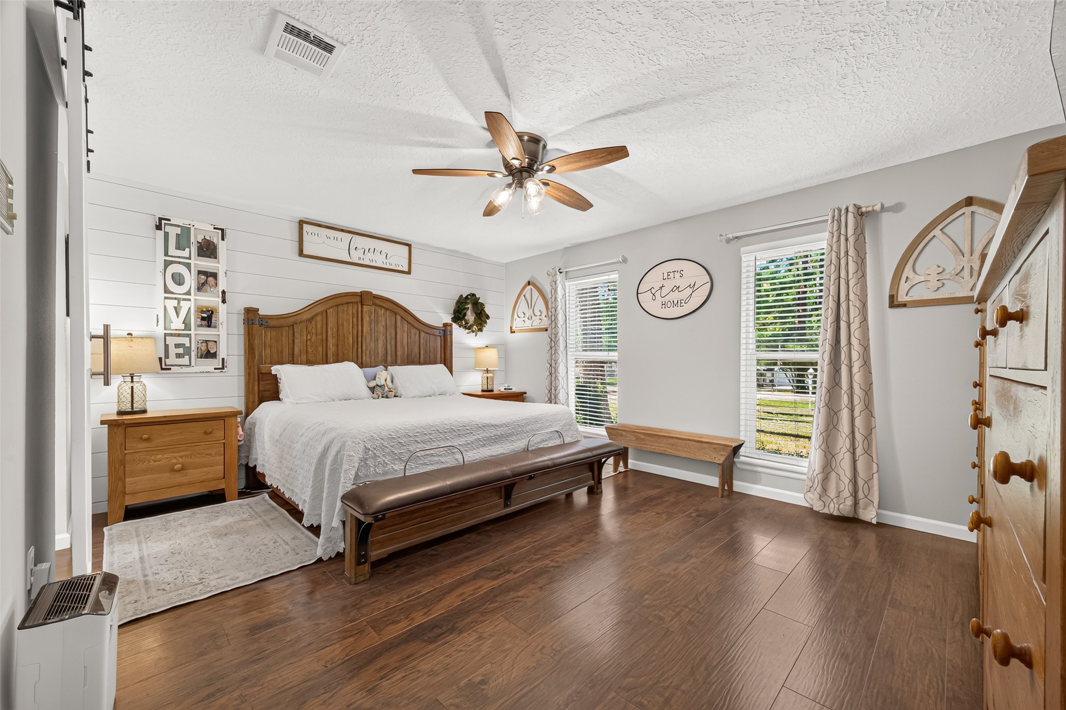 LOOK AT THIS SPACIOUS PRIMARY BEDROOM WITH THE ADDED SHIPLAP ACCENT WALL, BEAUTIFUL WOOD LIKE TILE FLOORS, LOTS OF NATURAL LIGHT; CURTAIN AND CURTAIN ROD WILL REMAIN WITH HOME