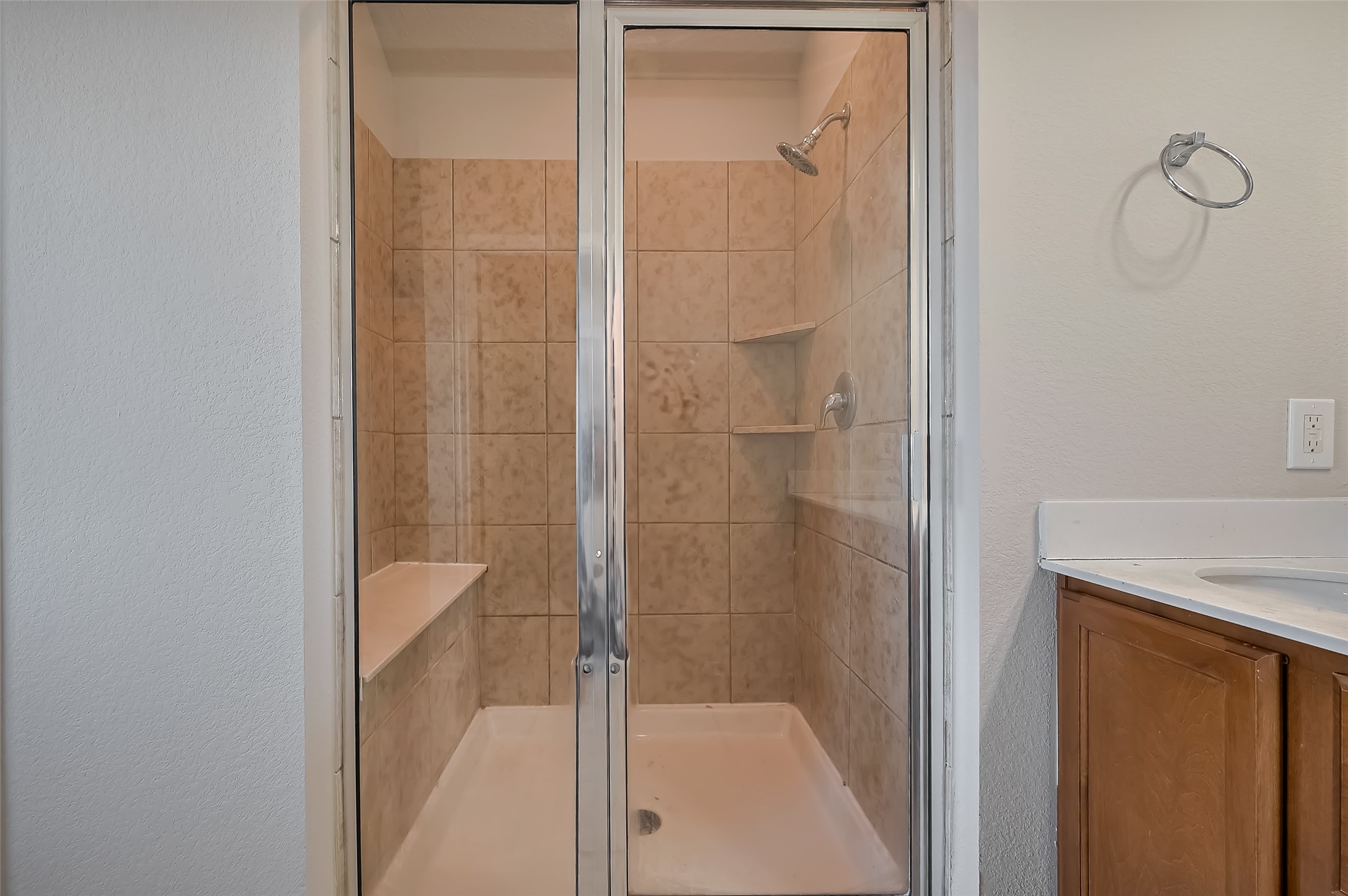 Shower with a glass door, built-in shelving, and a bench.