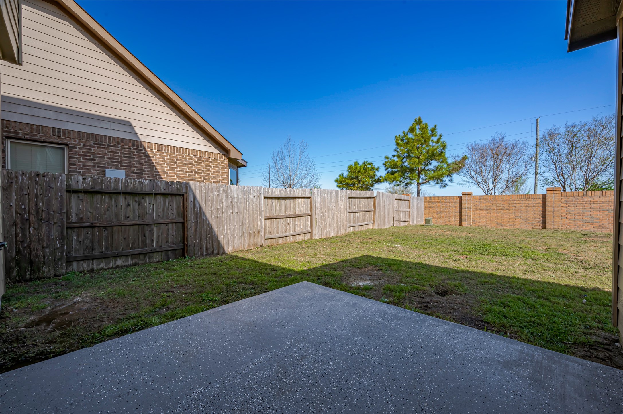 Spacious backyard with a concrete patio, wooden fencing.
