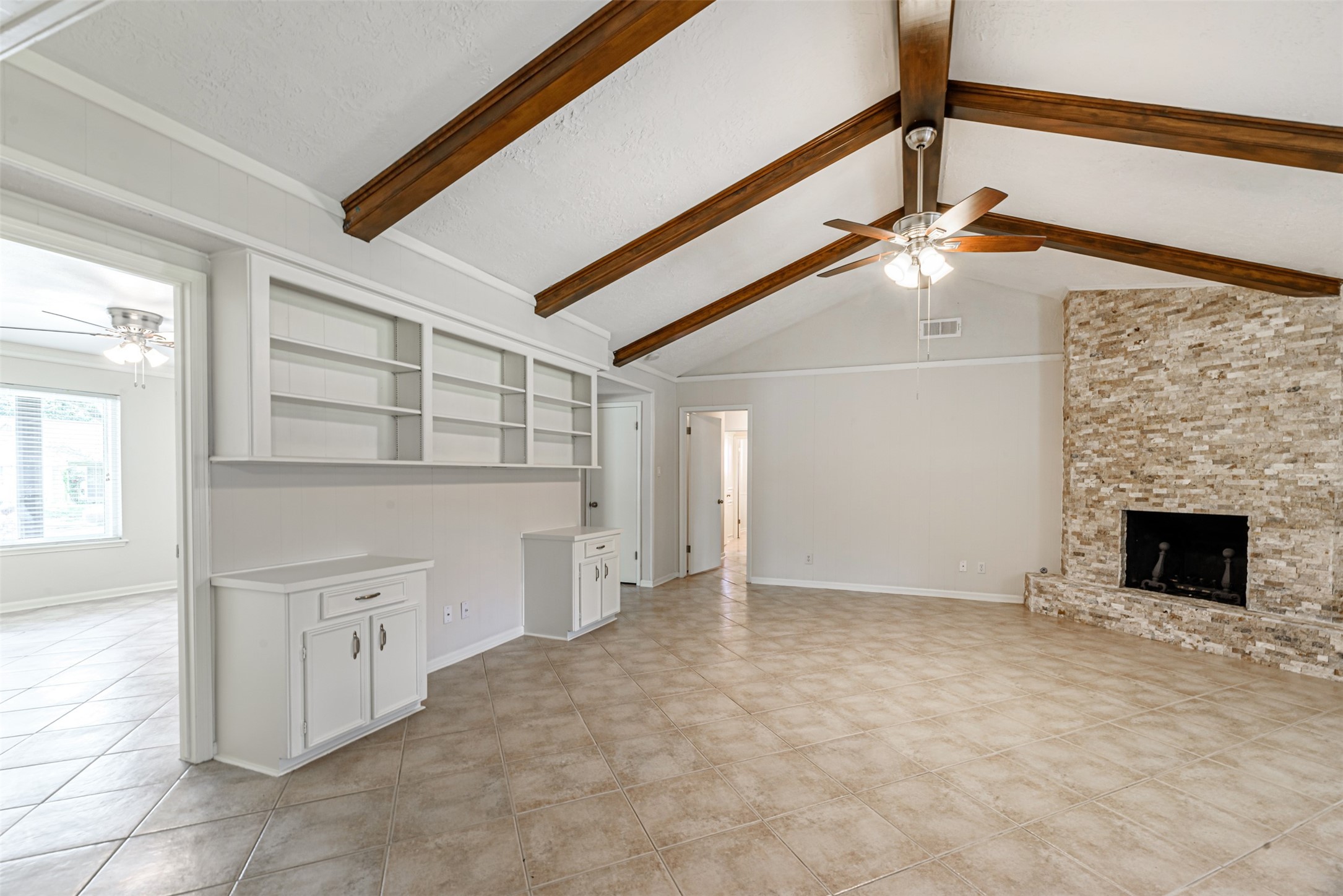 Step into the inviting formal living room through the access door on the left, featuring elegant wood-beamed ceilings, a cozy stone fireplace, and built-in shelving for a touch of sophistication. Step into the inviting formal living room through the access door on the left, featuring elegant wood-beamed ceilings, a cozy stone fireplace, and built-in shelving for a touch of sophistication.
