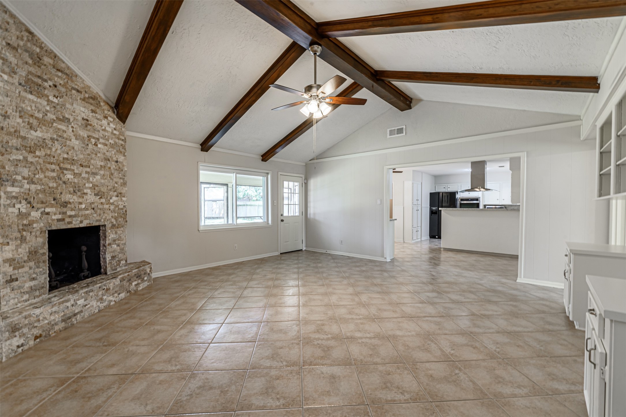 The expansive family room with its elegant beamed ceiling seamlessly flows into a modern kitchen, creating a perfect space for family gatherings.