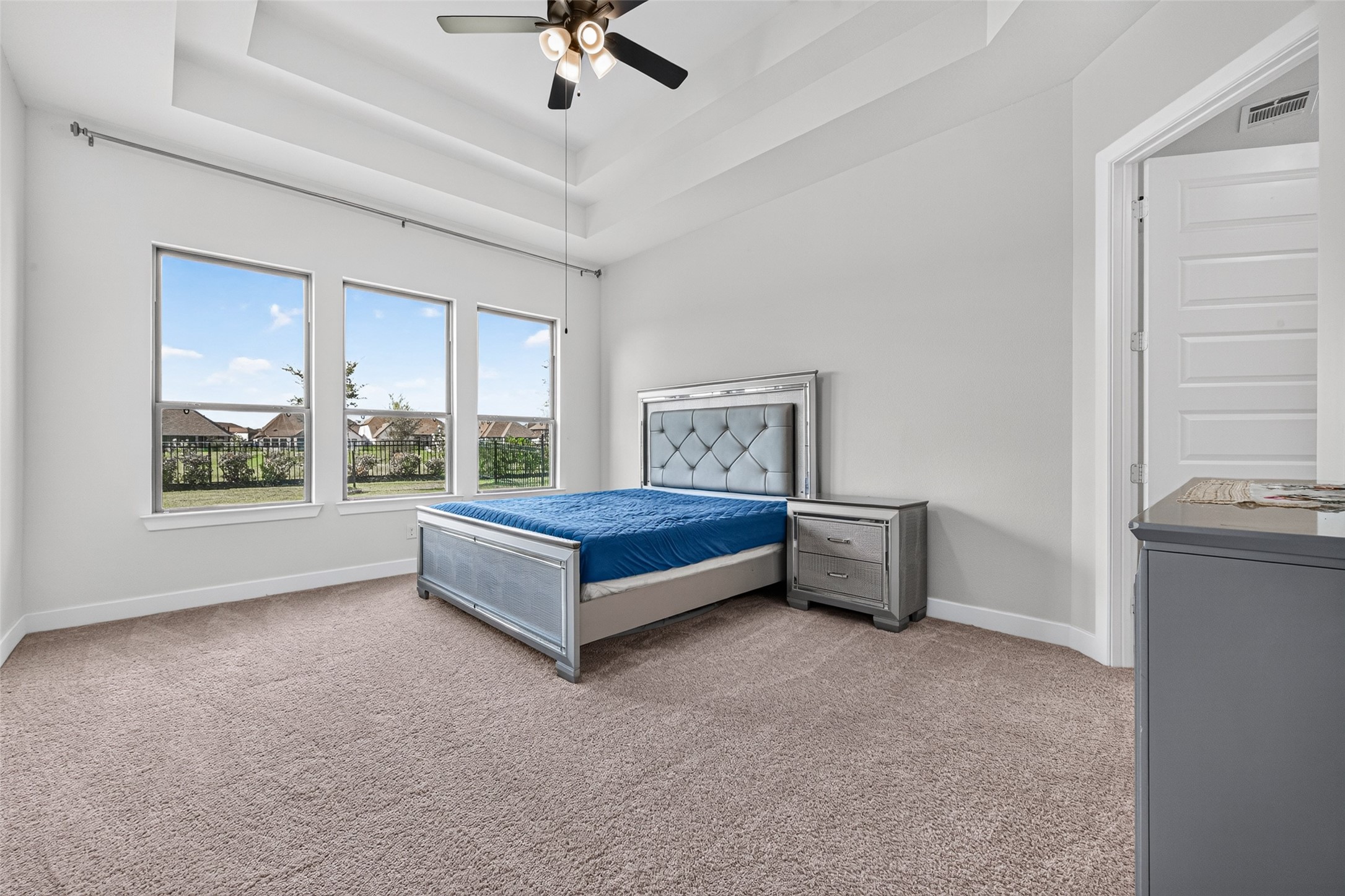 A luxurious primary bedroom featuring elegant tray ceilings and a stunning wall of windows, creating a spacious, sophisticated retreat filled with natural light and timeless appeal.