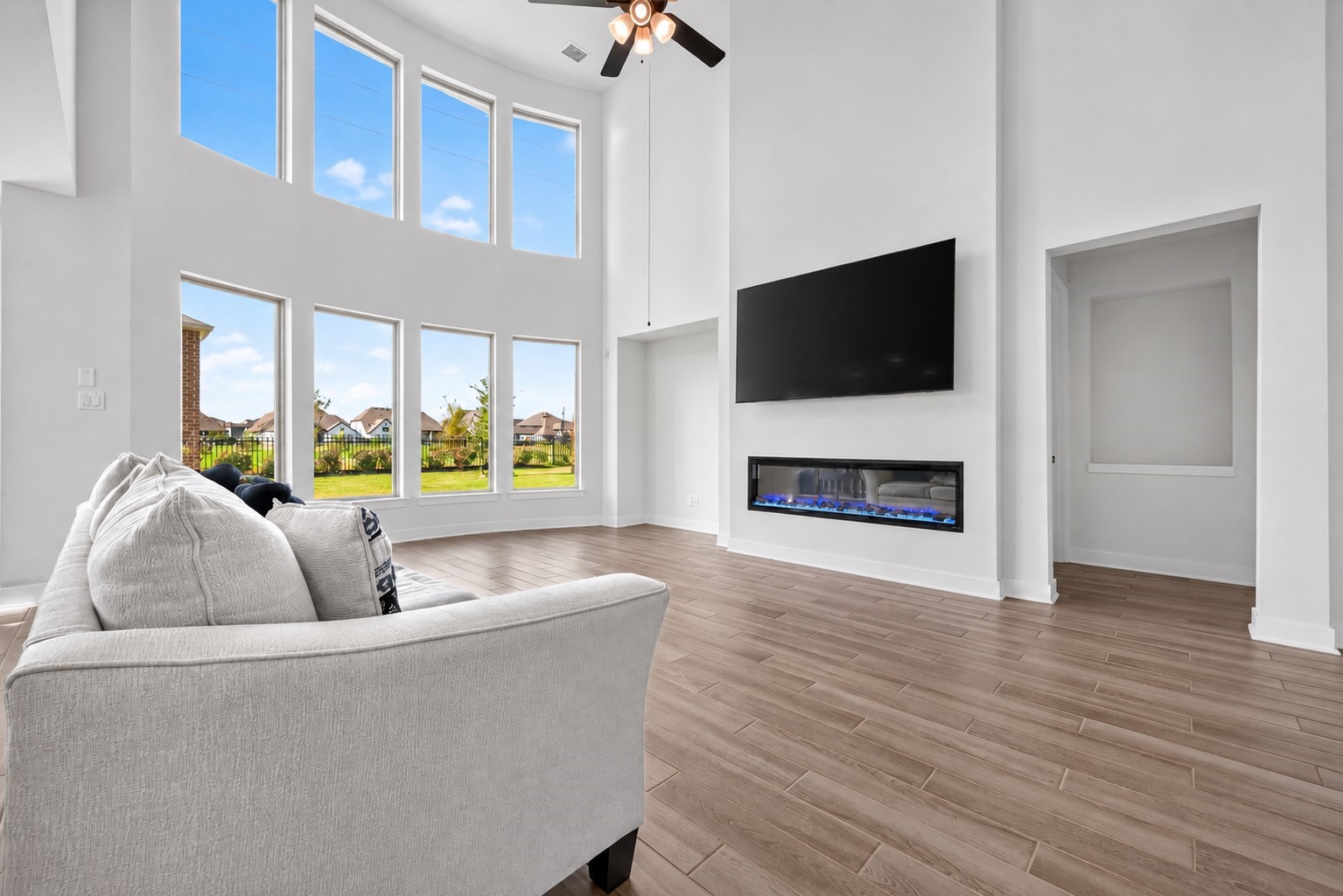 A grand, open-concept living space featuring soaring ceilings, a dramatic wall of windows, and a sleek electric fireplace that sets the scene for elegant entertaining, cozy evenings, and unforgettable moments in a truly inviting atmosphere