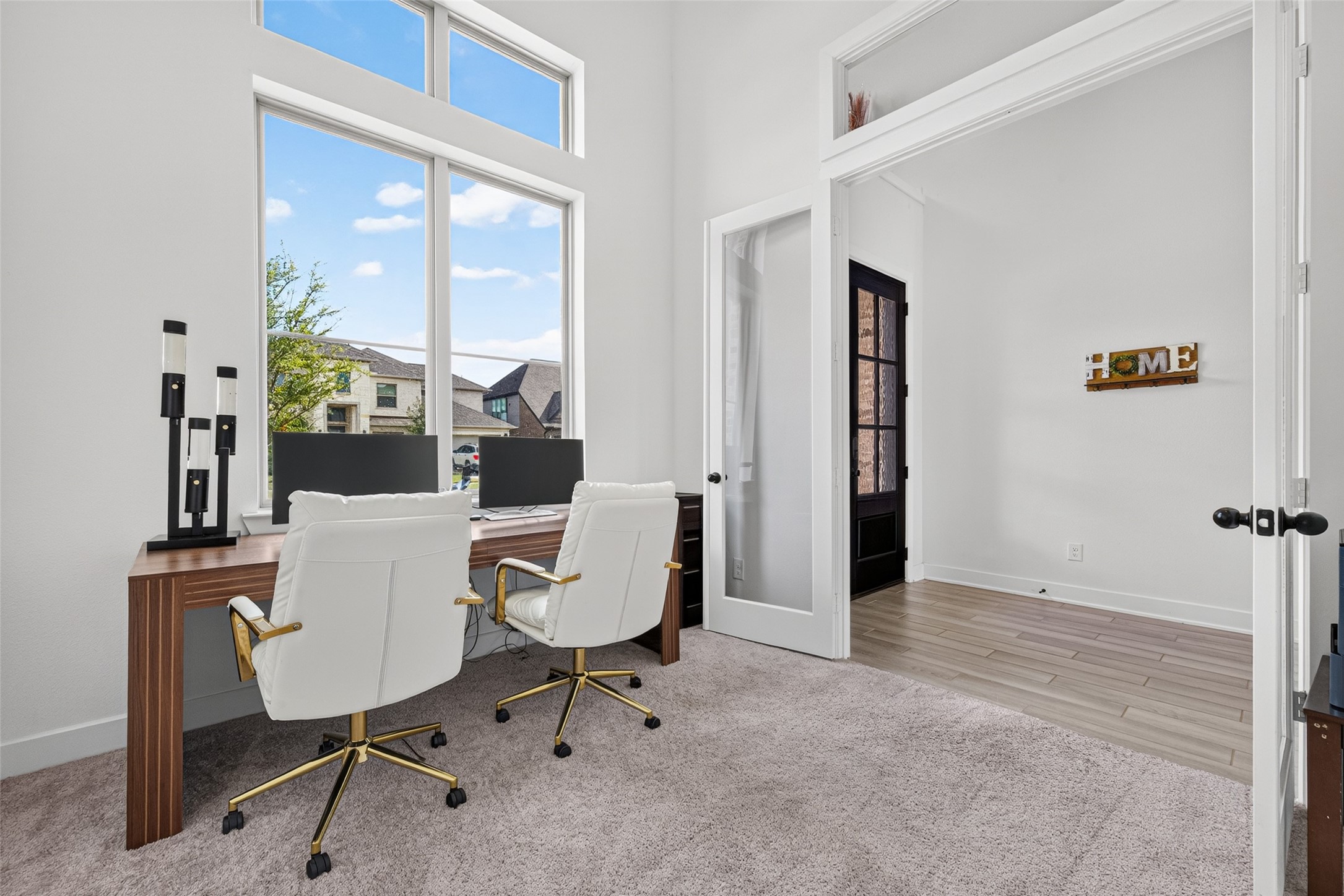 A distinguished executive-style home office featuring elegant glass French doors and a dramatic wall of windows, creating a refined, light-filled workspace that exudes luxury and sophistication