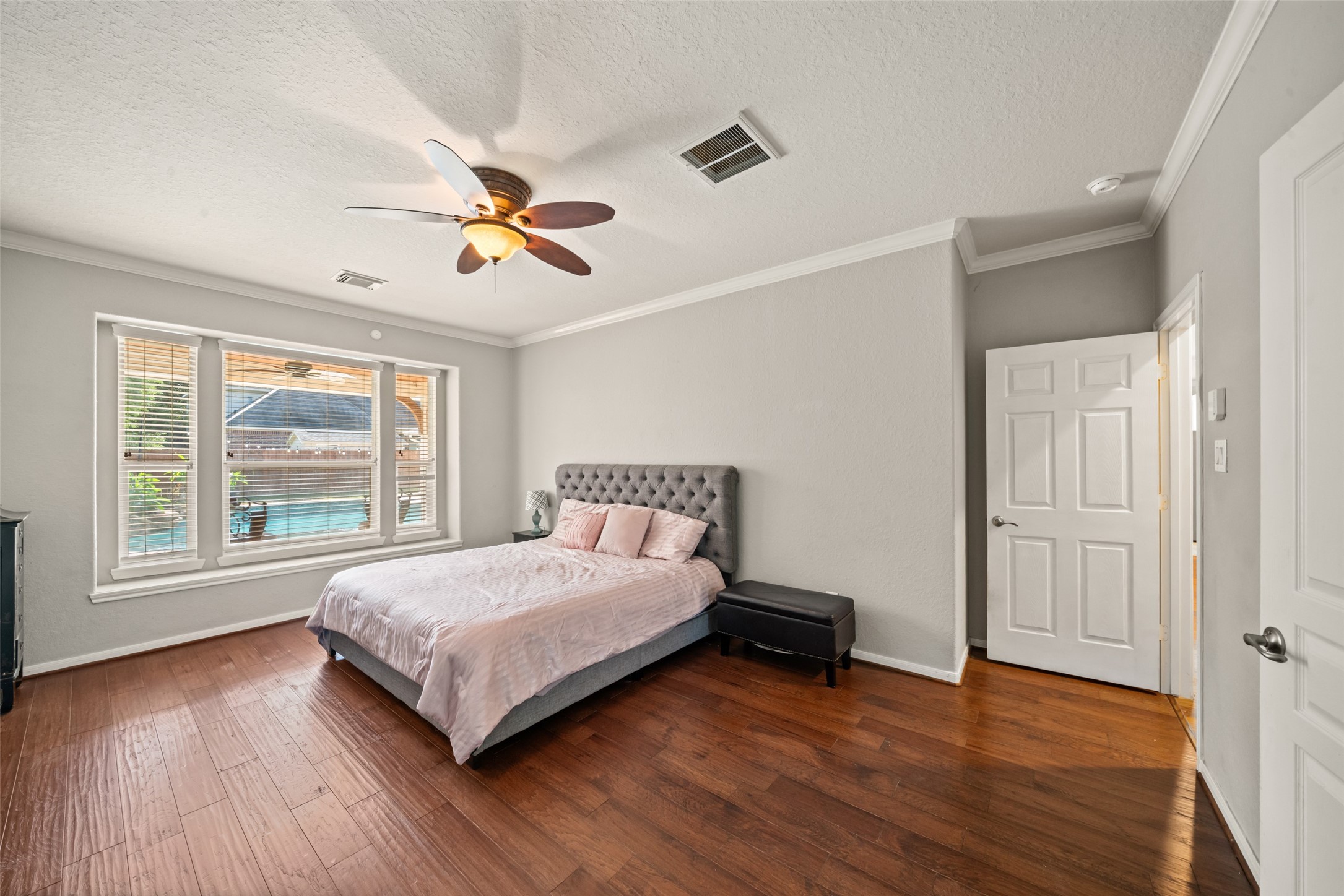 A spacious primary bedroom with natural lighting and view of the sparkling pool.