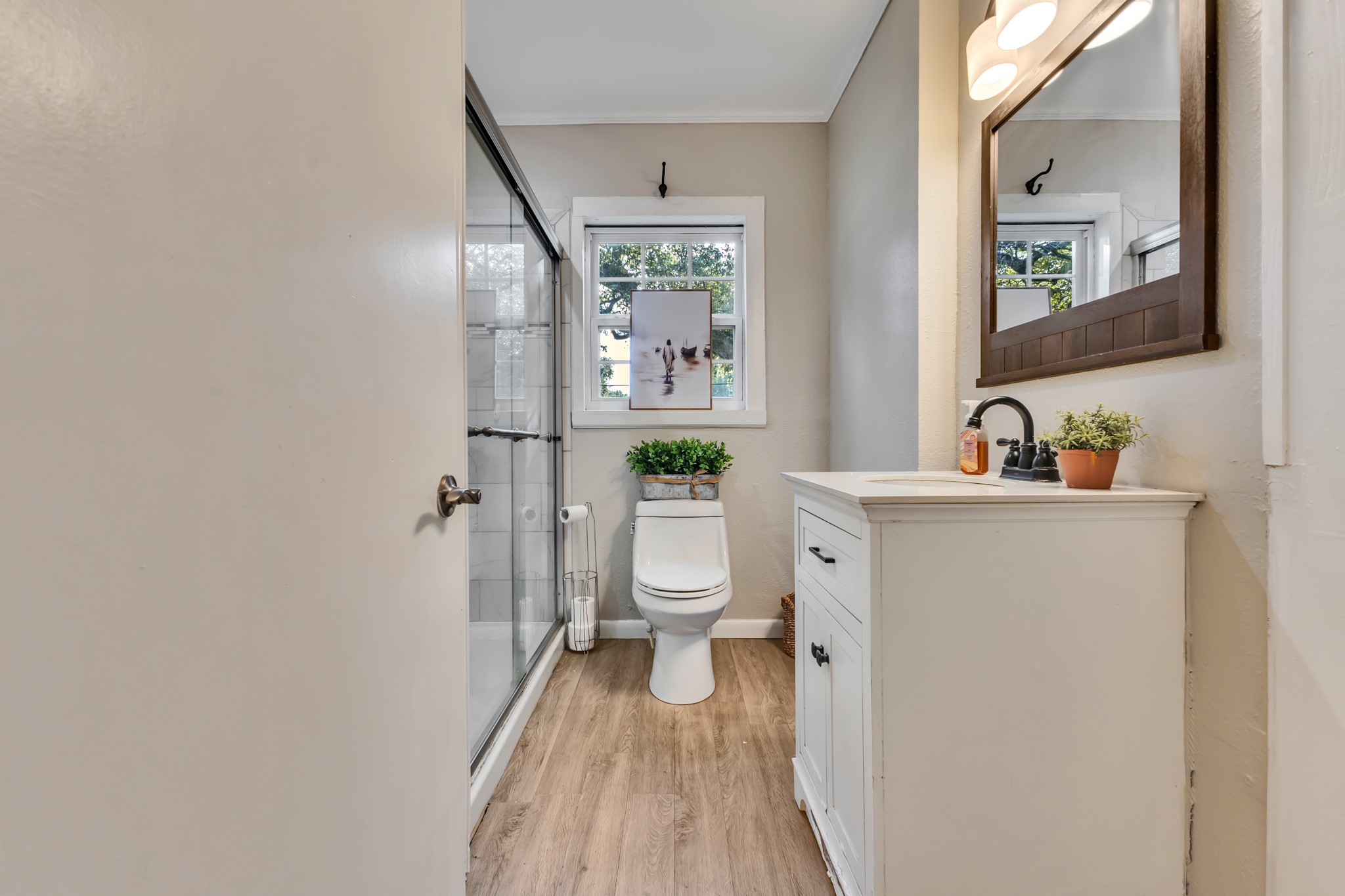 The bathroom features a tiled shower with glass doors, a white vanity, and wood-look flooring. These attractive finishes provide a fresh, welcoming appearance that complements the rest of the home's interior.