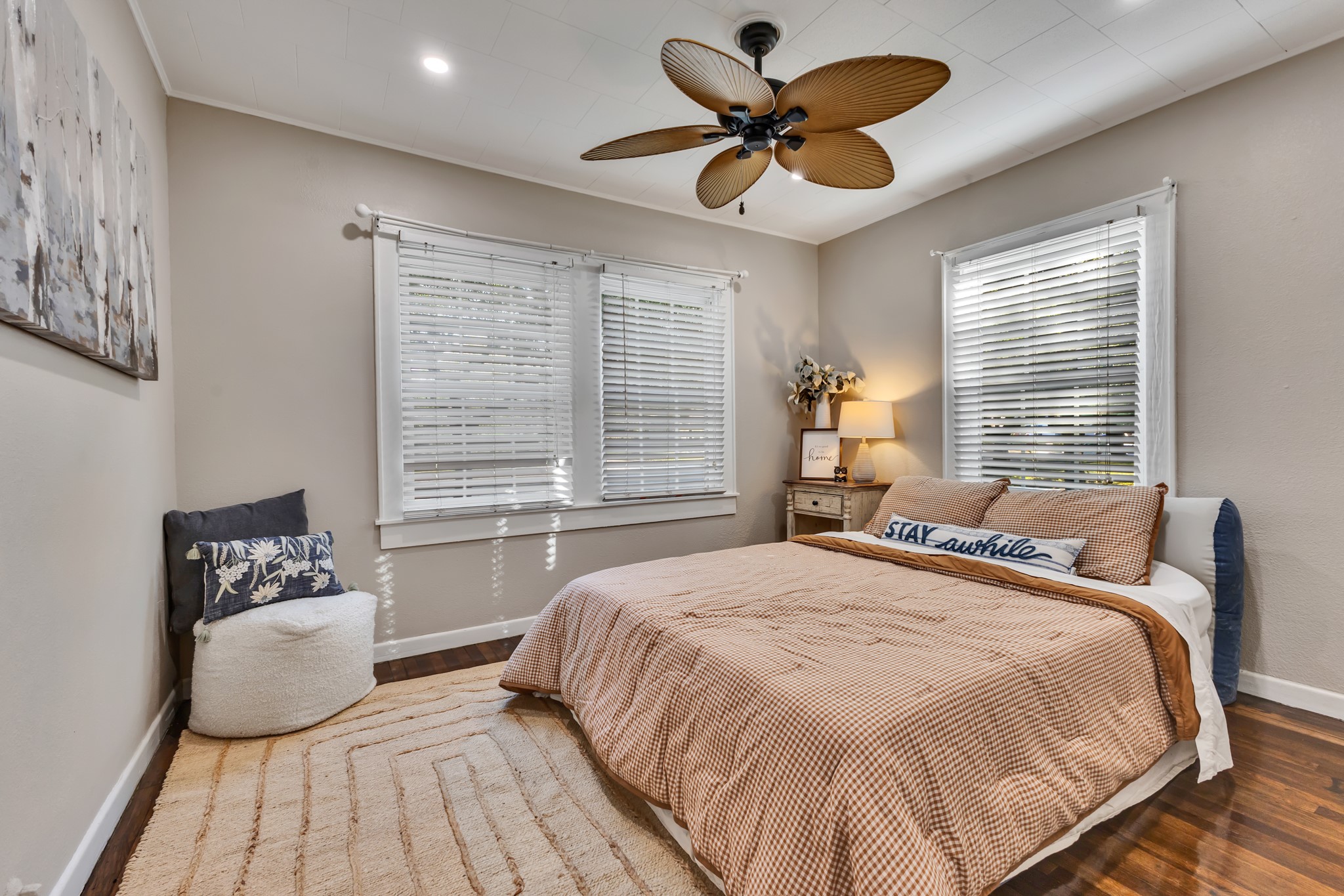 A comfortable primary bedroom with beautiful wood flooring, natural light, and a ceiling fan. Its neutral finishes provide a versatile foundation for creating a relaxing personal space without requiring a complete style overhaul.