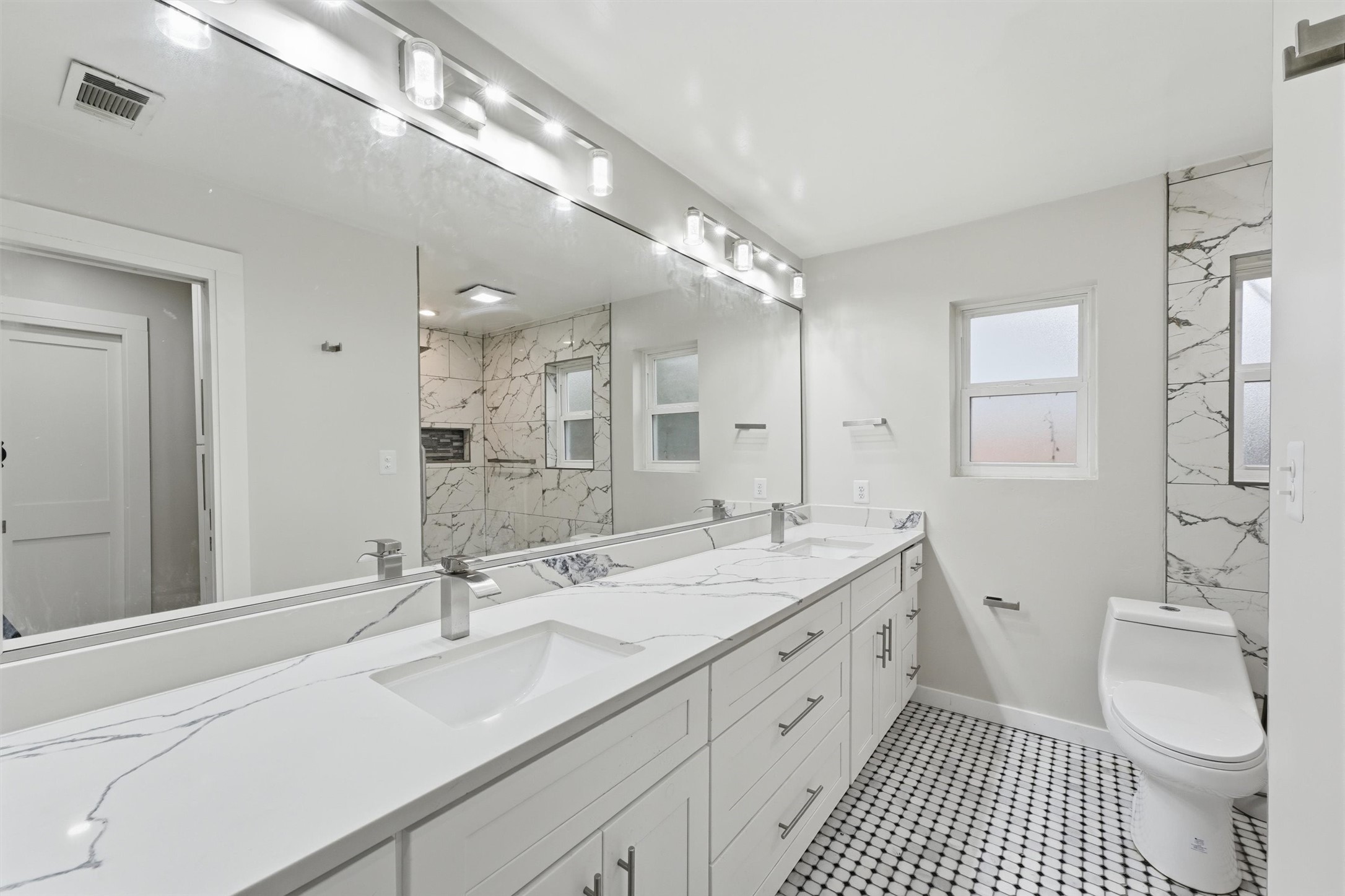 The third bathroom offers a double vanity with generous counterspace and storage, a large wall mirror, and patterned black-and-white tile flooring.