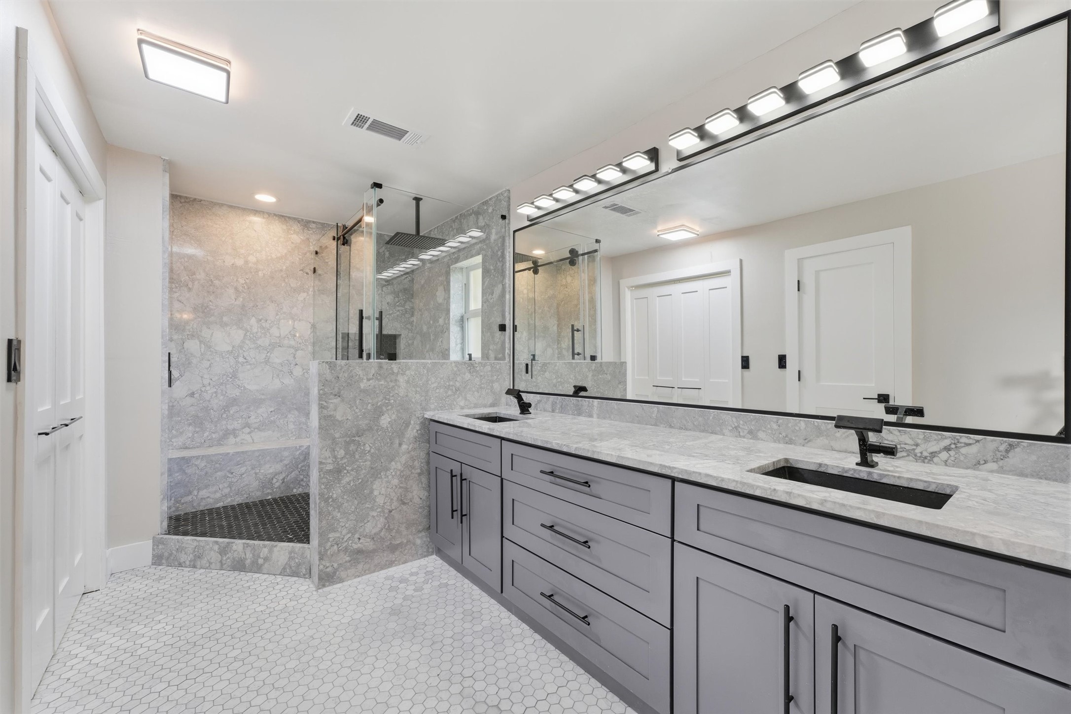 The second primary suite's private bathroom features a double vanity with black fixtures, a tub and shower combination with a glass enclosure, quartzite walls, and plenty of cabinet storage.