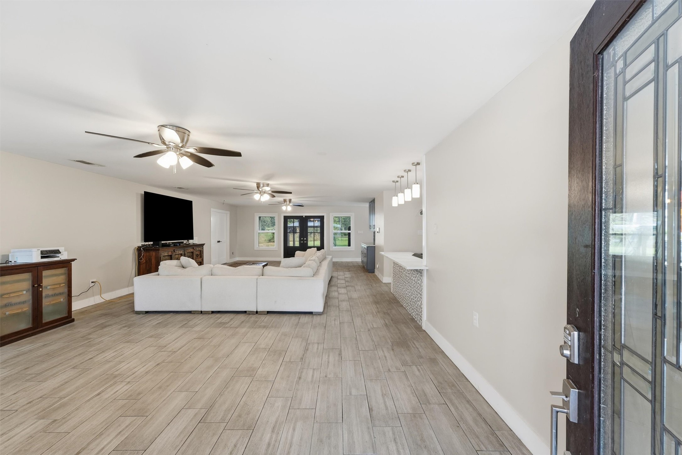 Spacious, open-concept living area with wood-like tile flooring, ceiling fans, and a clear view into kitchen and dining area.