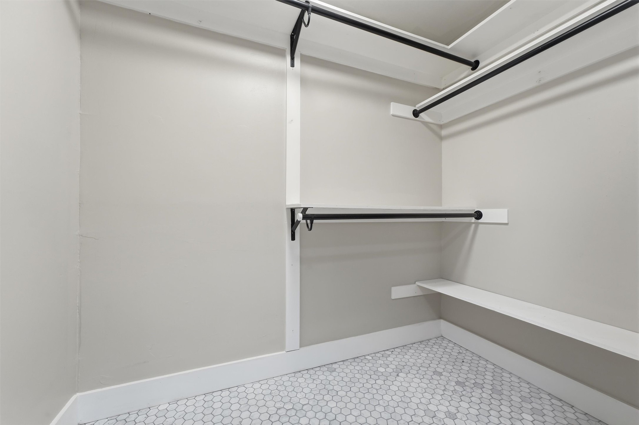 The second primary suite includes a walk-in closet conveniently located off the bathroom, with multiple hanging rods, storage shelves, and hexagonal tile flooring.