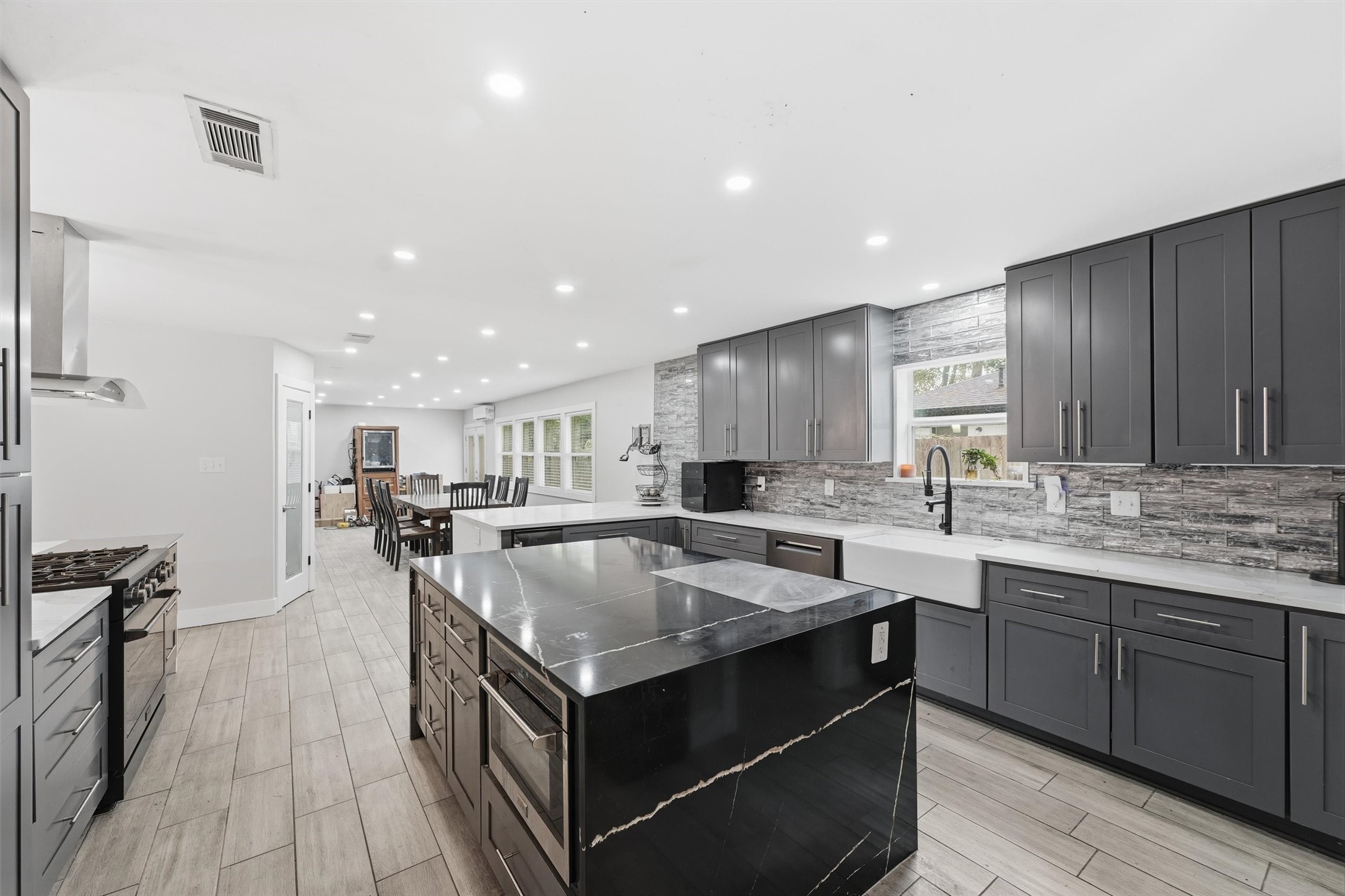 The center island features a contrasting dark quartzite countertop, built-in microwave, and additional storage, while quartz countertops and a farmhouse-style sink complete the back wall of the kitchen.