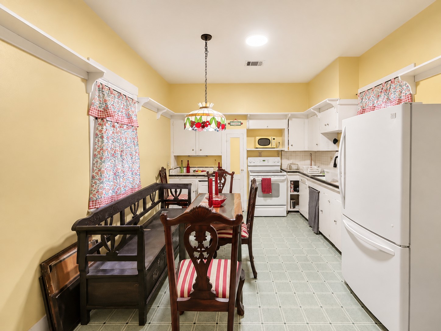 Spacious eat-in kitchen features abundant white cabinetry, generous counter space, and a dedicated dining area beneath a colorful pendant light. Warm yellow walls and crisp white trim add cheerful character.