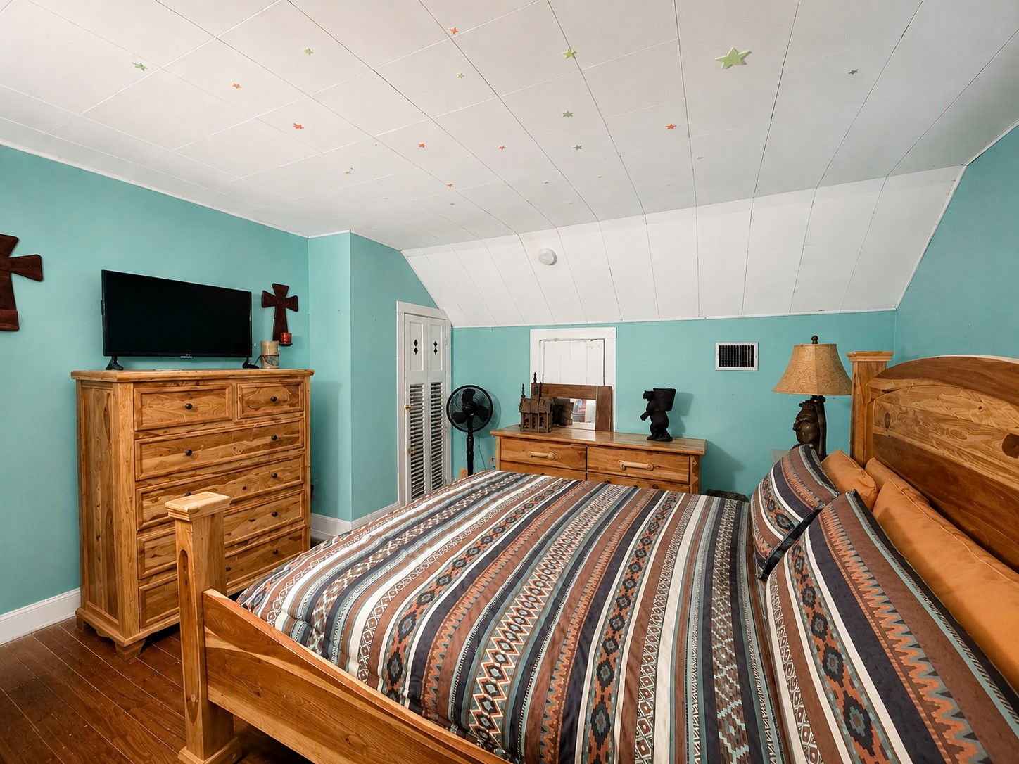 Spacious bedroom features warm wood flooring, turquoise walls, and a distinctive sloped ceiling that adds architectural character. Classic white trim provides a crisp contrast throughout the room.