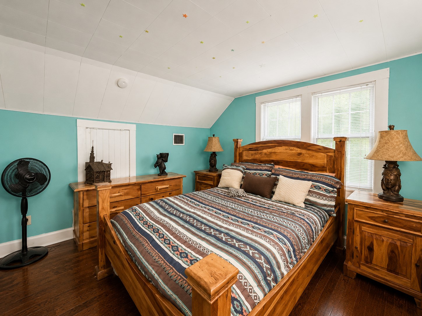 Multiple windows brighten the bedroom while the sloped ceiling and wood flooring enhance its character. The spacious footprint comfortably accommodates substantial furnishings.